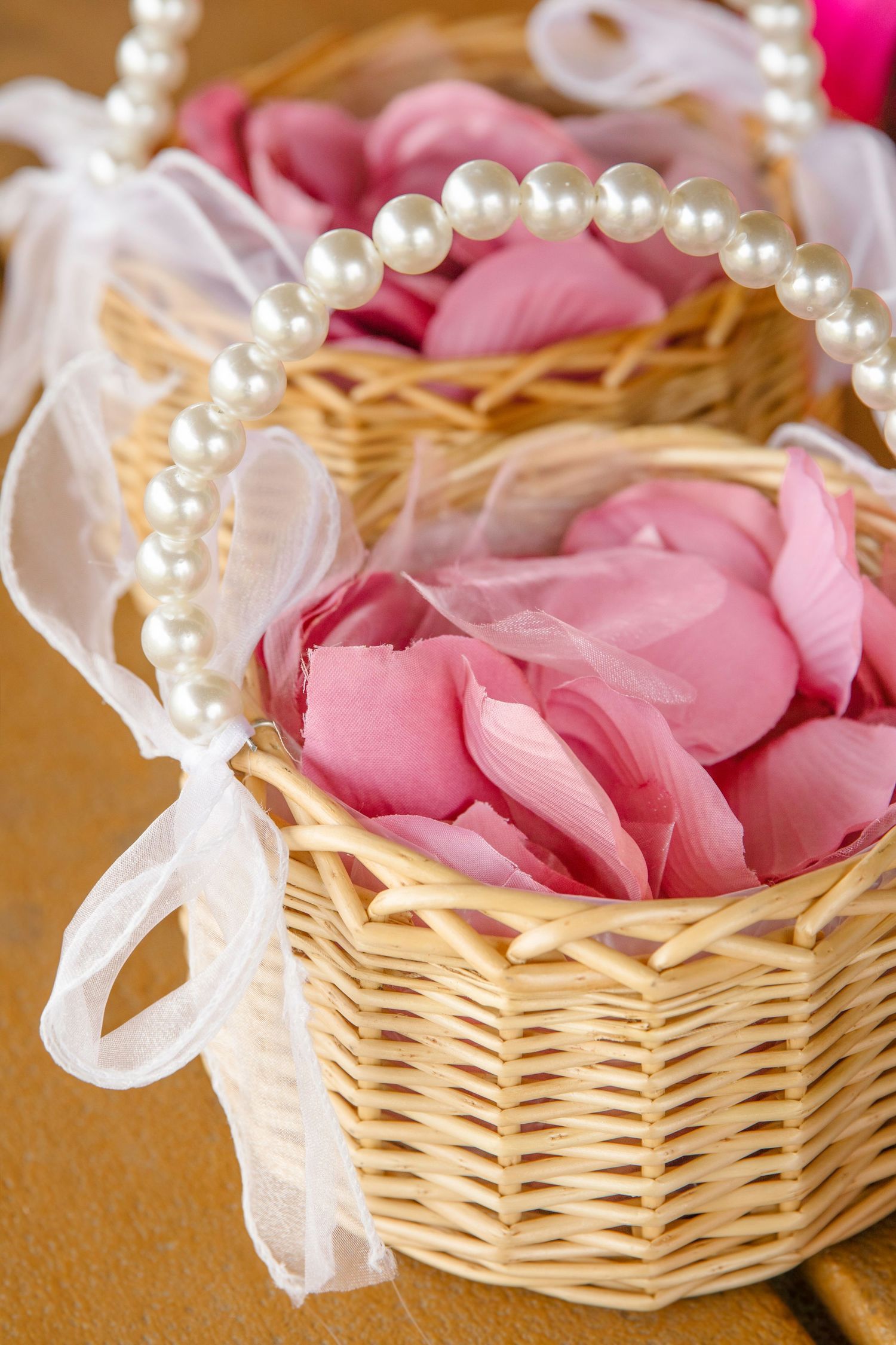Woven basket filled with pink rose petals decorated with a pearl necklace.
