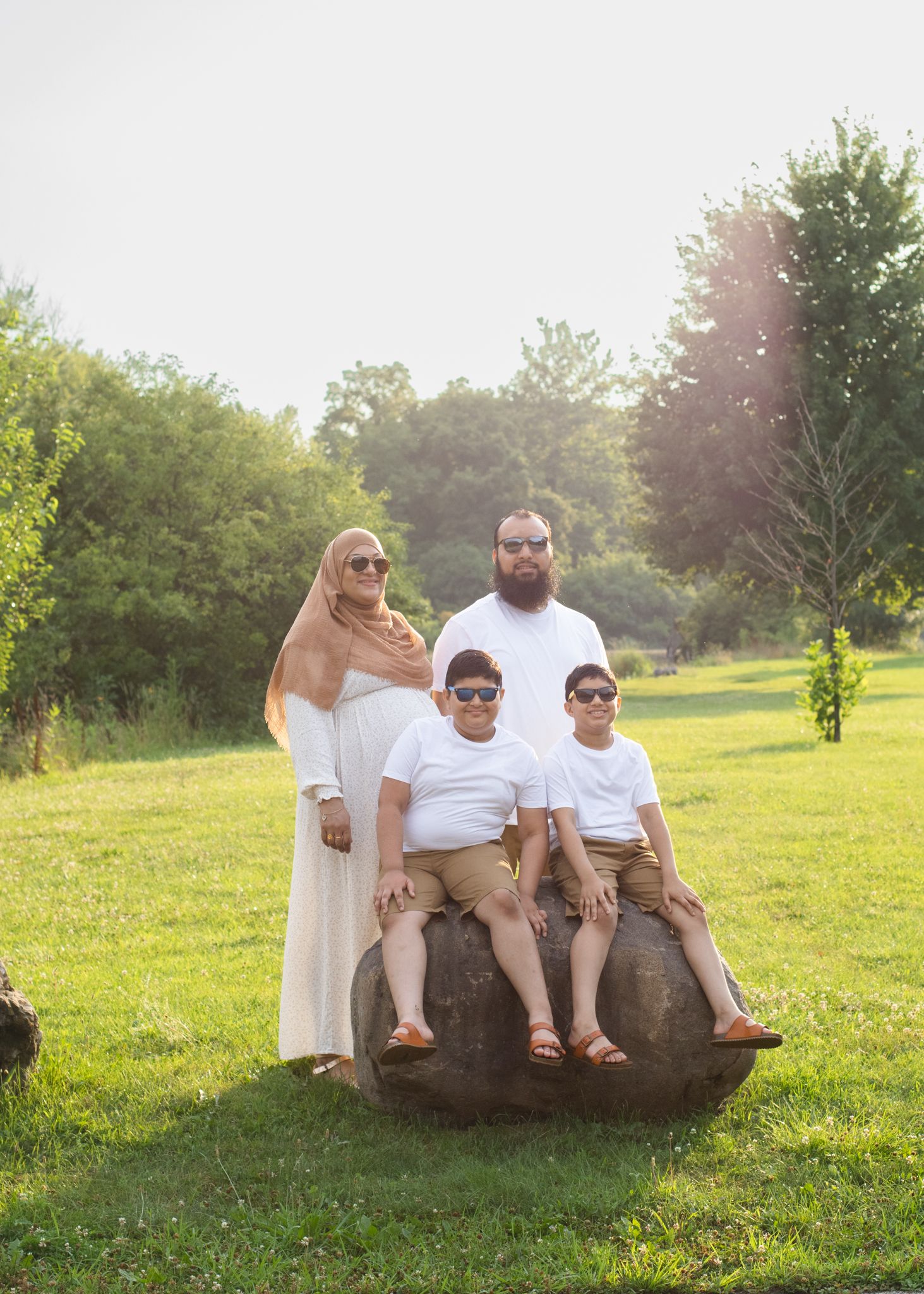 Family poses casually on decorative rock in sunny park setting.