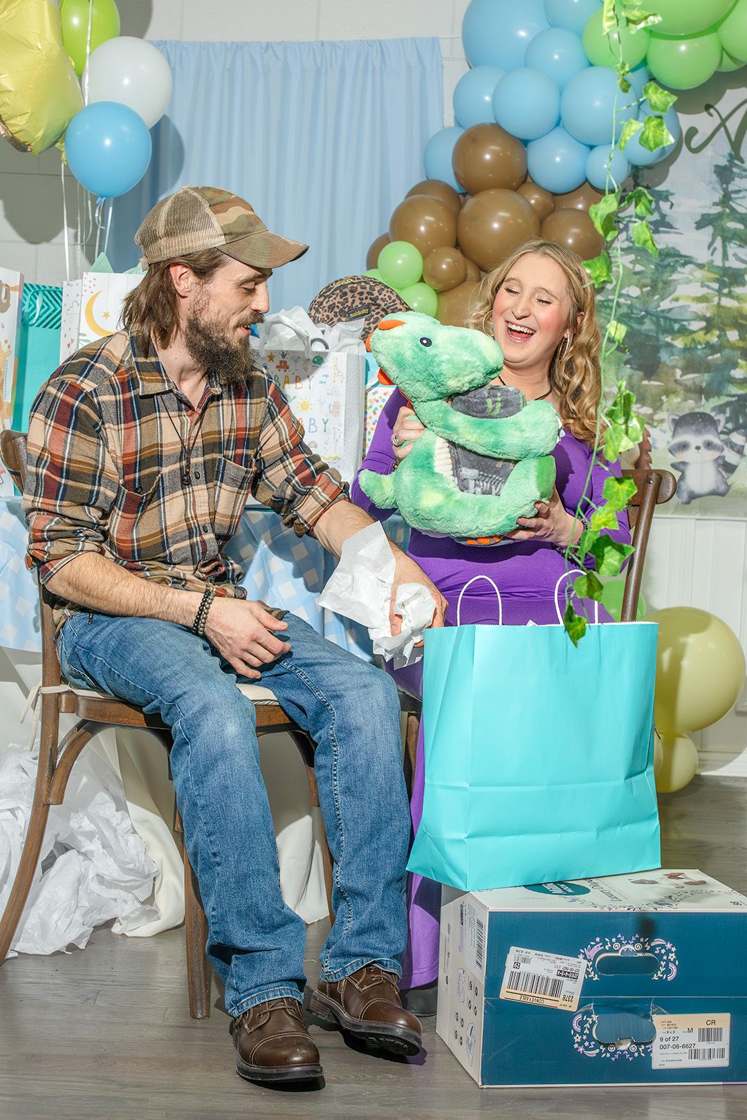 A couple shares a joyful moment at a baby shower with balloons, gifts and a plush toy dragon among the decorations.