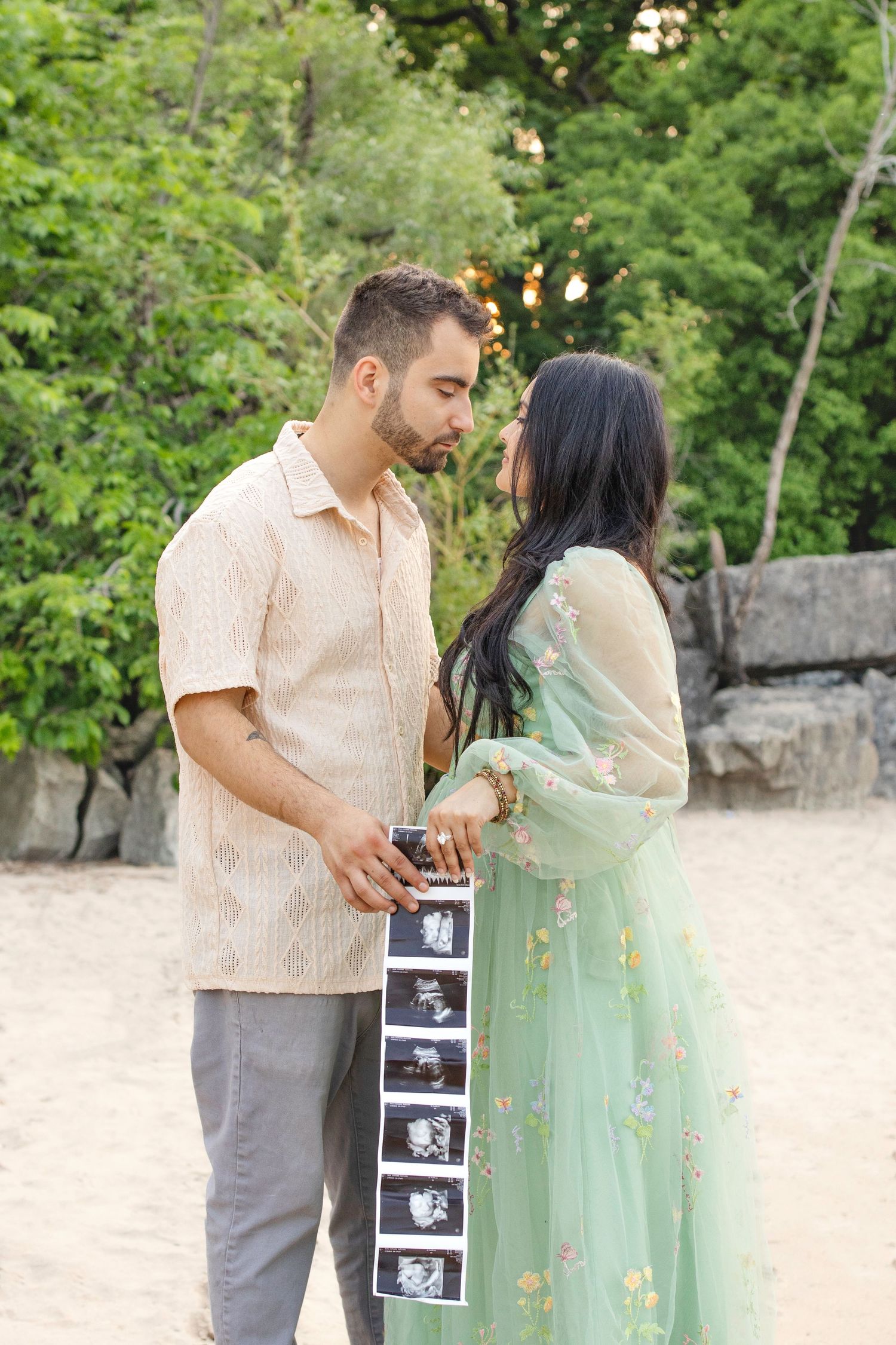 A couple holding ultrasound photos together outdoors while dressed in pastel colors during a pregnancy announcement photoshoot.