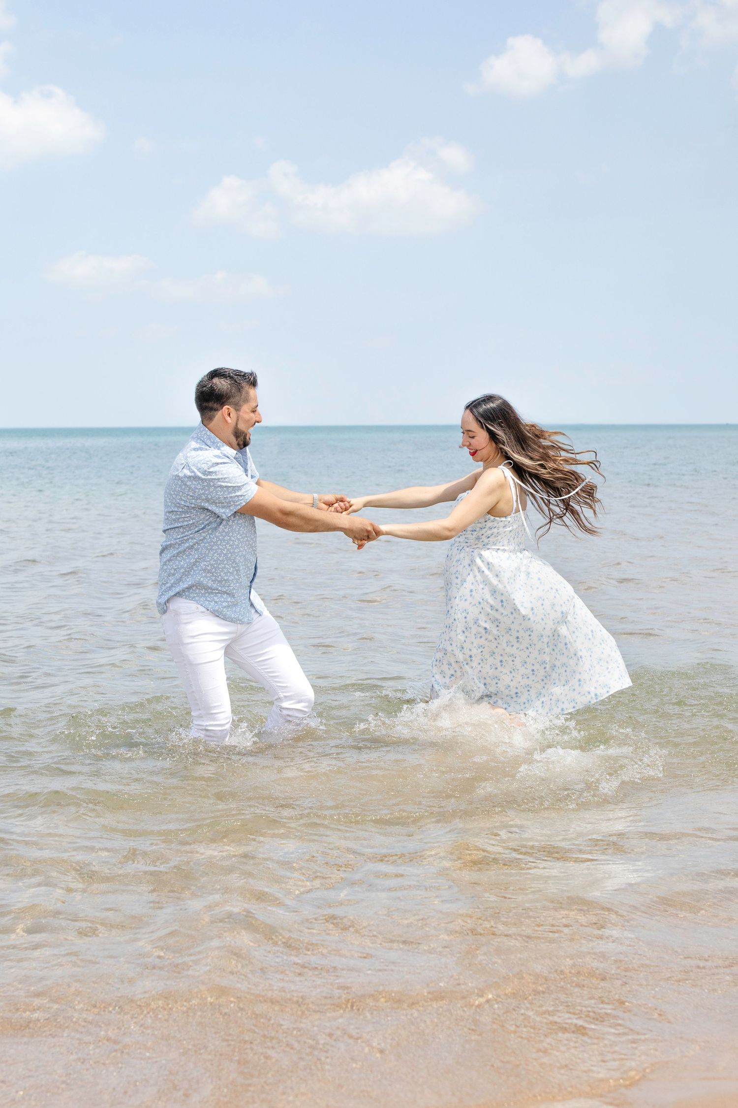 Couple dancing and splashing playfully in the shallow ocean water at beach during a sunny day.
