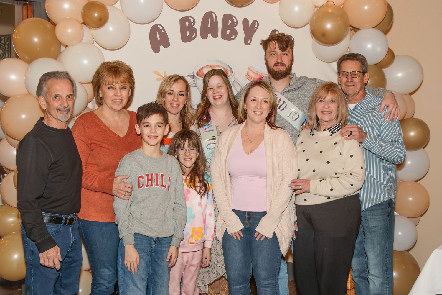Family group photo at a baby shower with balloon arch backdrop featuring neutral beige and white balloons.
