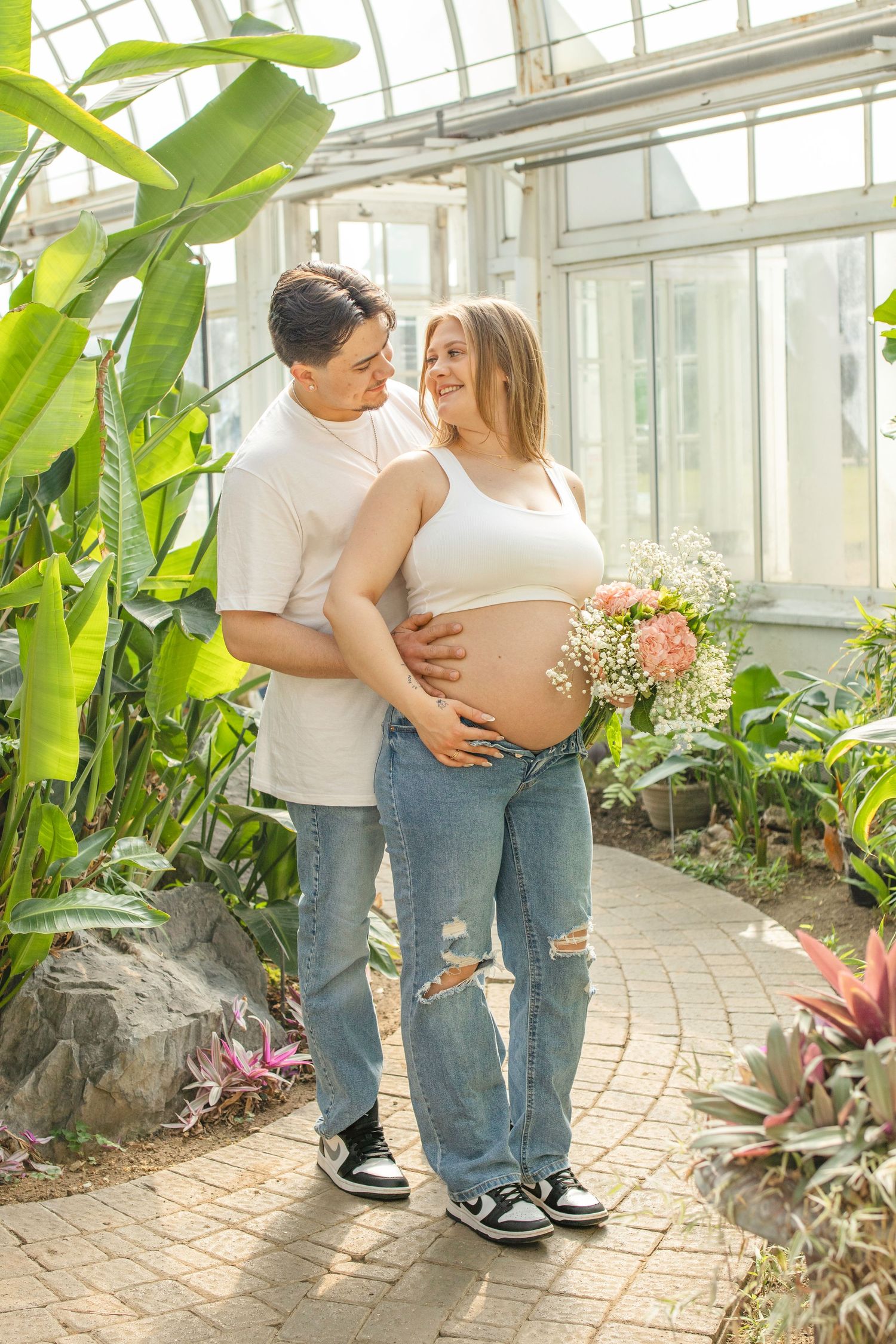 Couple embraces in natural greenhouse setting with tropical plants and flowers.