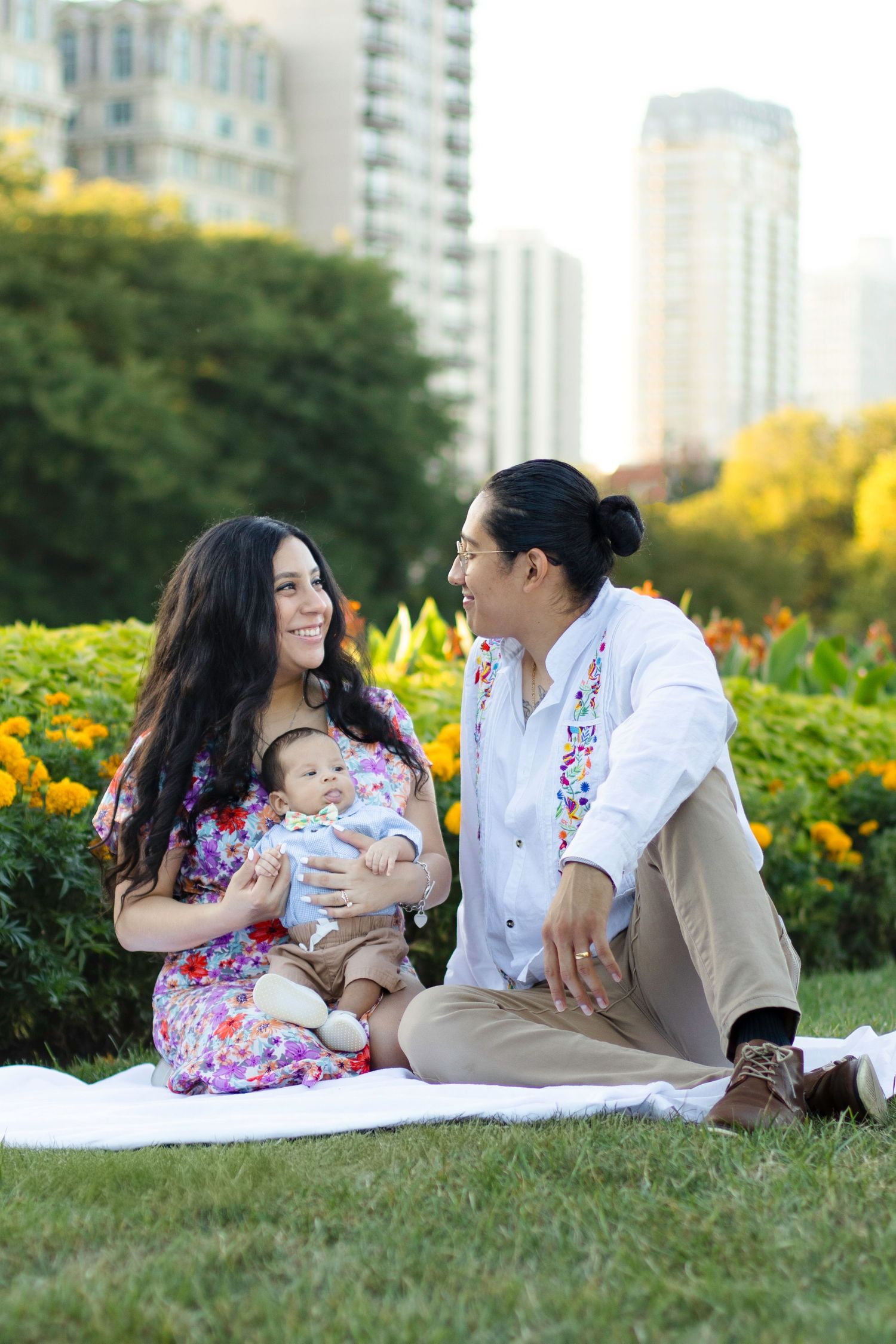 Family relaxes on blanket in urban garden with city buildings visible in background.