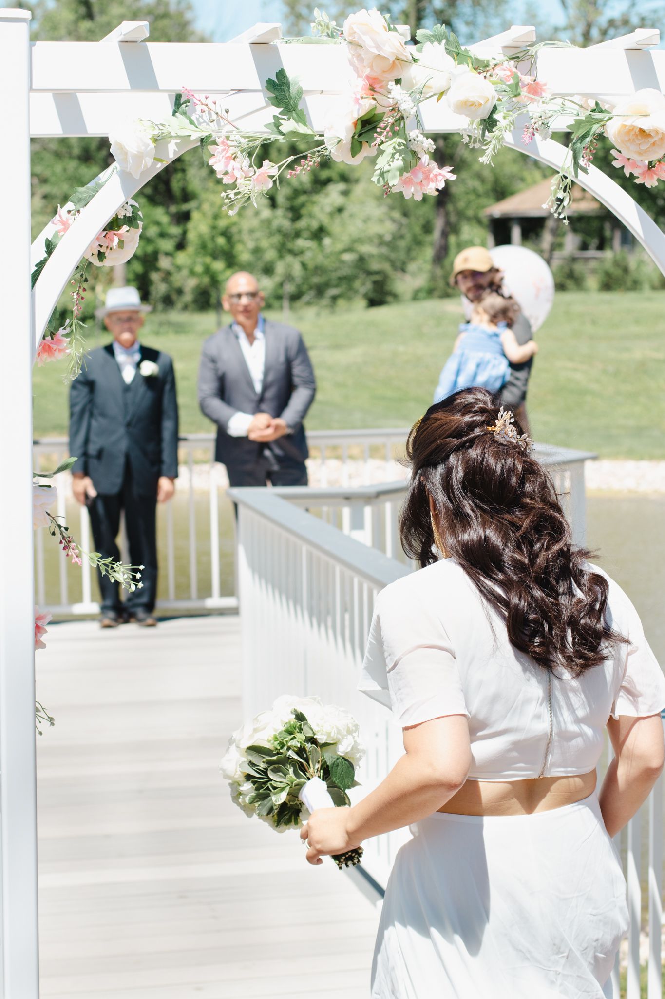 Wedding ceremony setup with floral arch and pink roses under sunny skies.