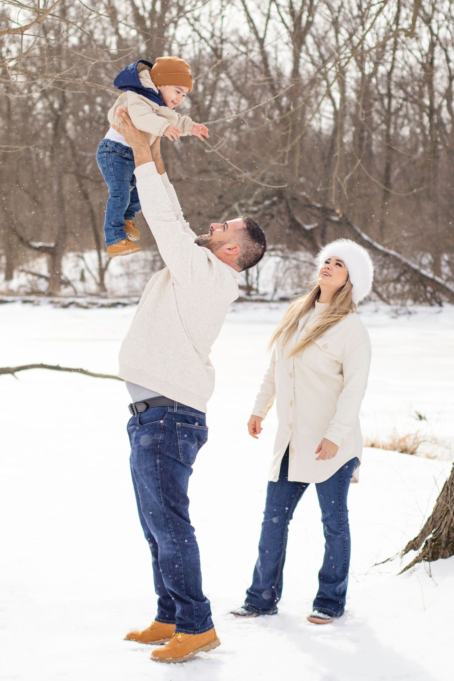 Family playing in snowy winter scene with child being lifted high.