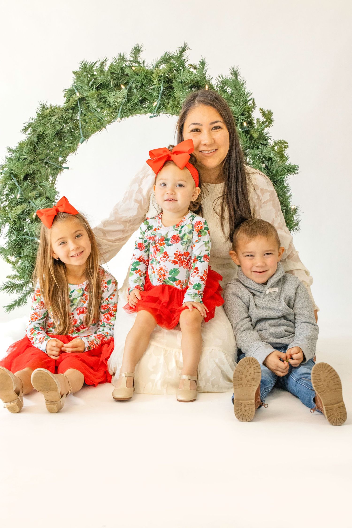 Family members lying down in matching holiday attire with floral prints and red bows against a white backdrop.