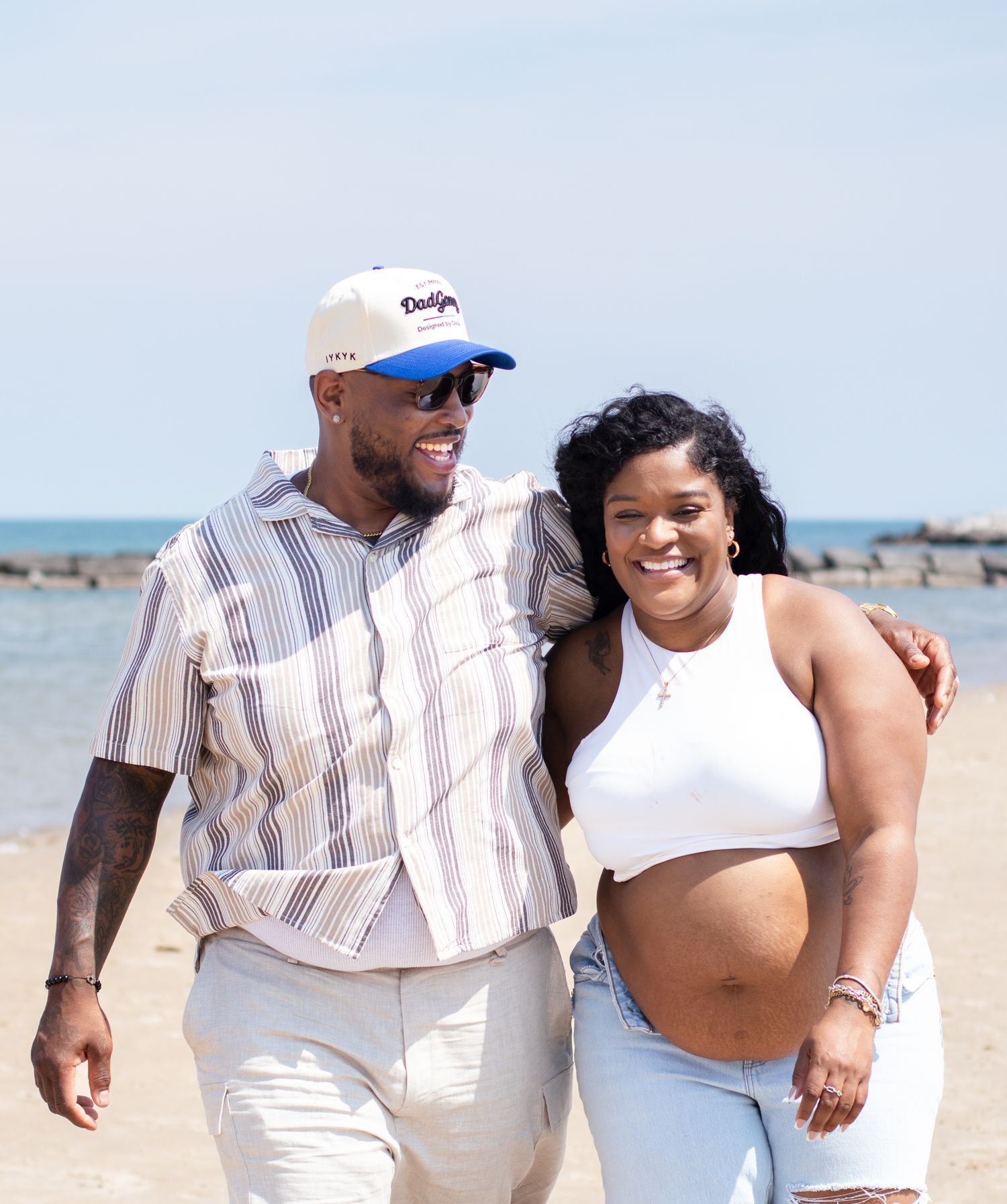Happy couple embracing on beach with rocky shoreline and blue water in background.