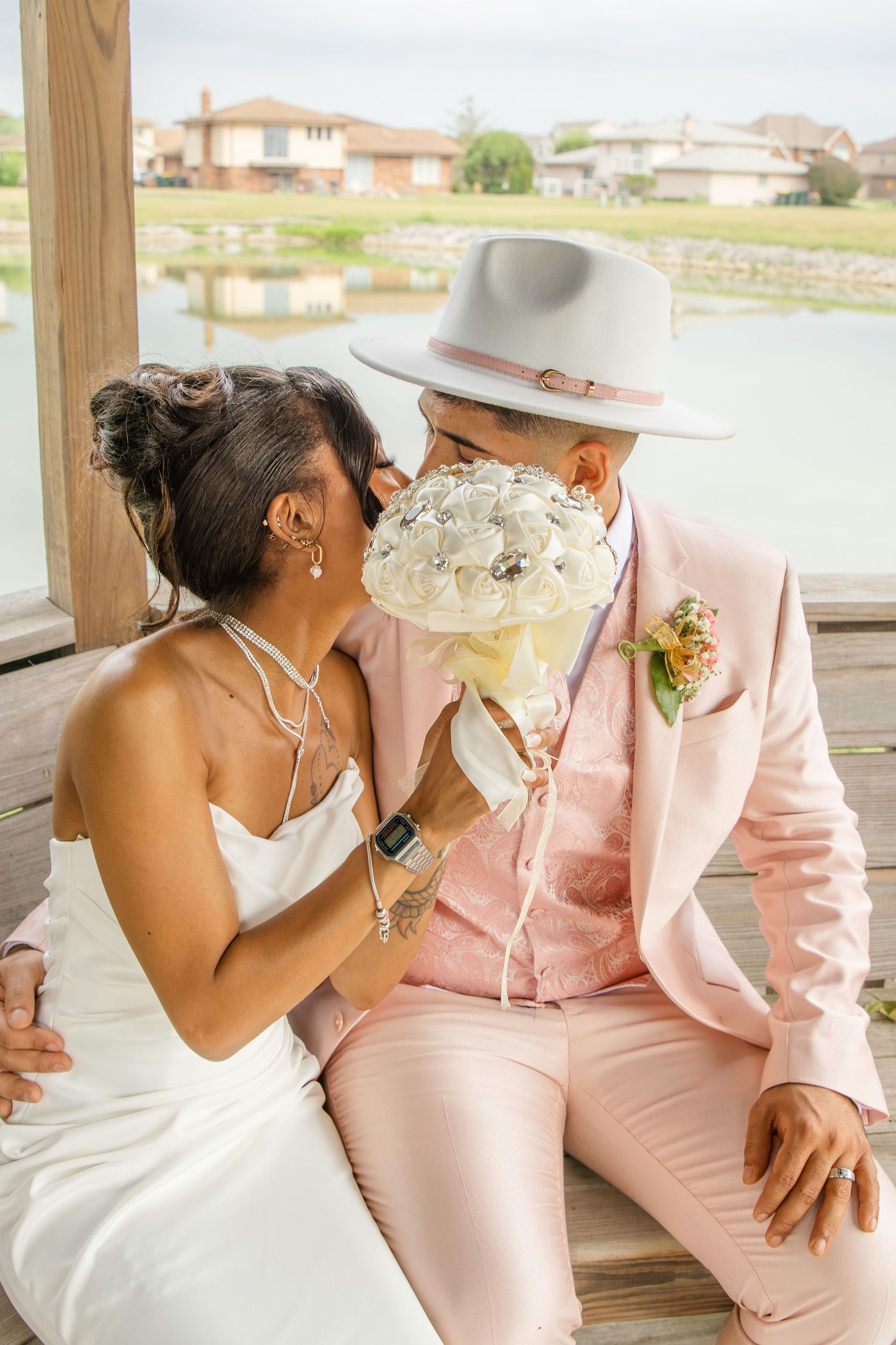 A tender wedding moment on a porch with the couple in white dress and pink suit sharing a floral bouquet.