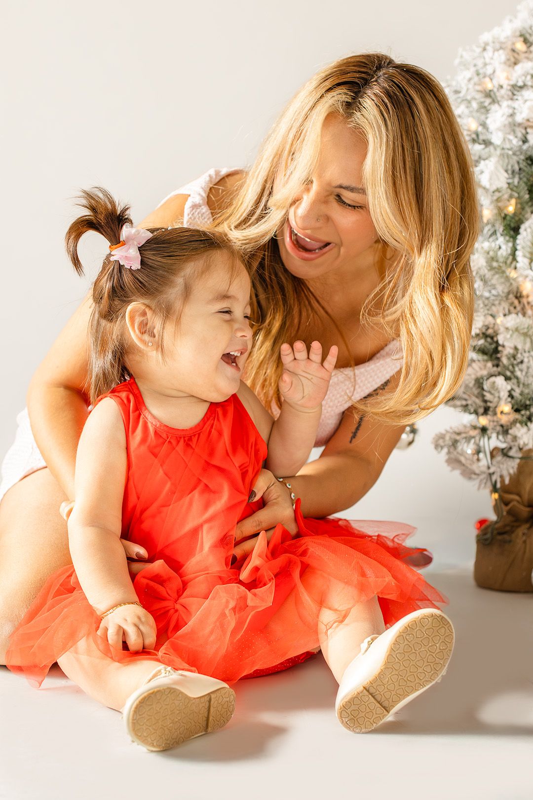 A parent and child in matching coral outfits share tender moments while laying on a white floor with blossoms nearby.