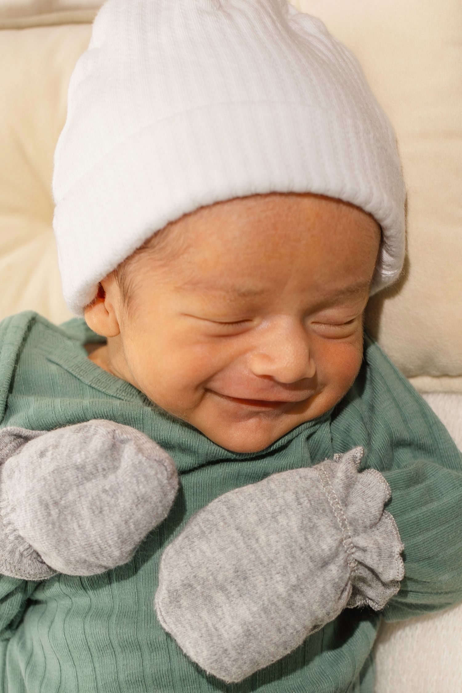 A sleeping newborn baby wearing a white hat, mint green outfit, and gray bow tie rests peacefully.