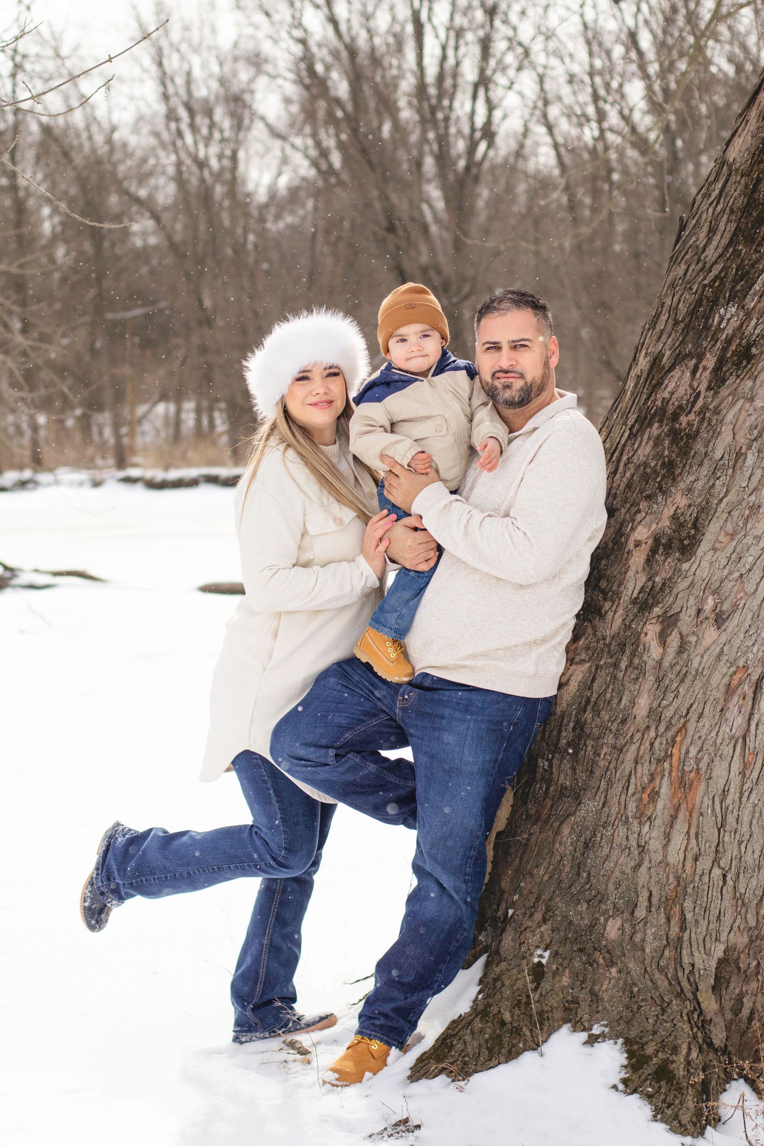 Winter family portrait against large tree trunk in snowy forest.