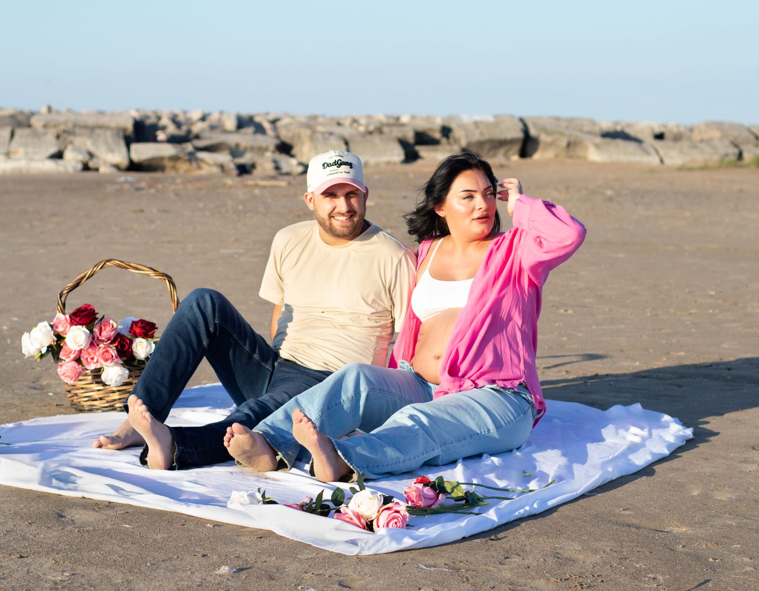 Couple enjoying beach picnic with floral basket and blanket setup.