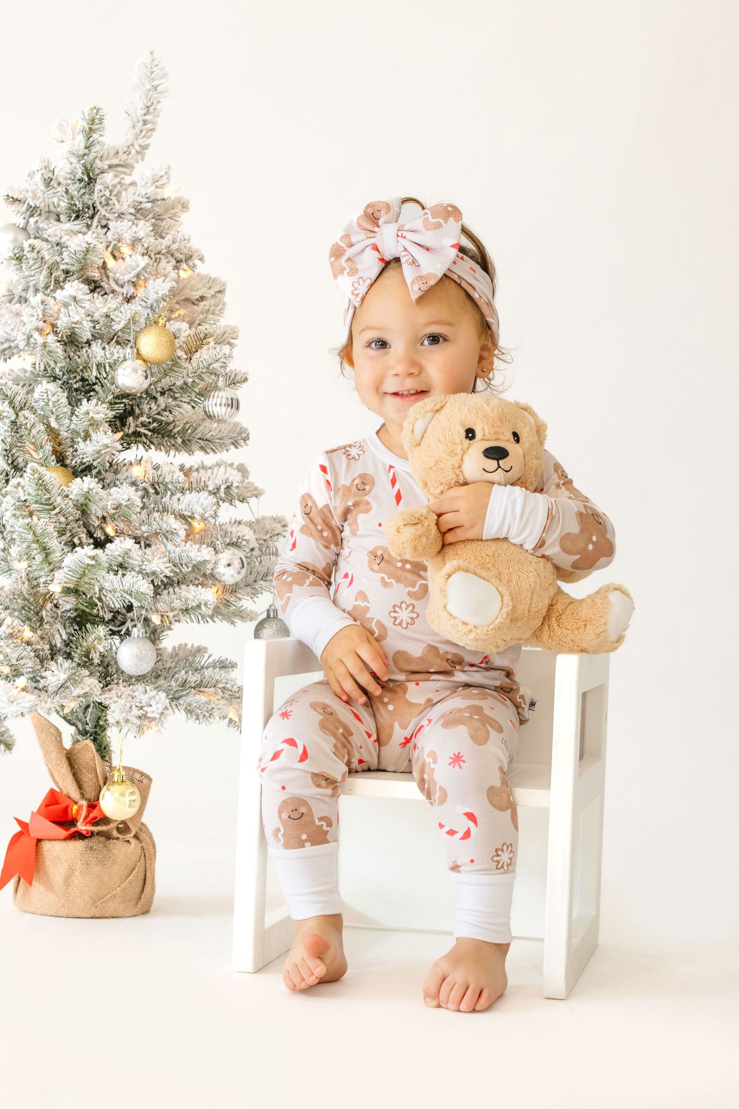 Holiday themed photo with a decorated white Christmas tree, teddy bear, and matching floral outfits.