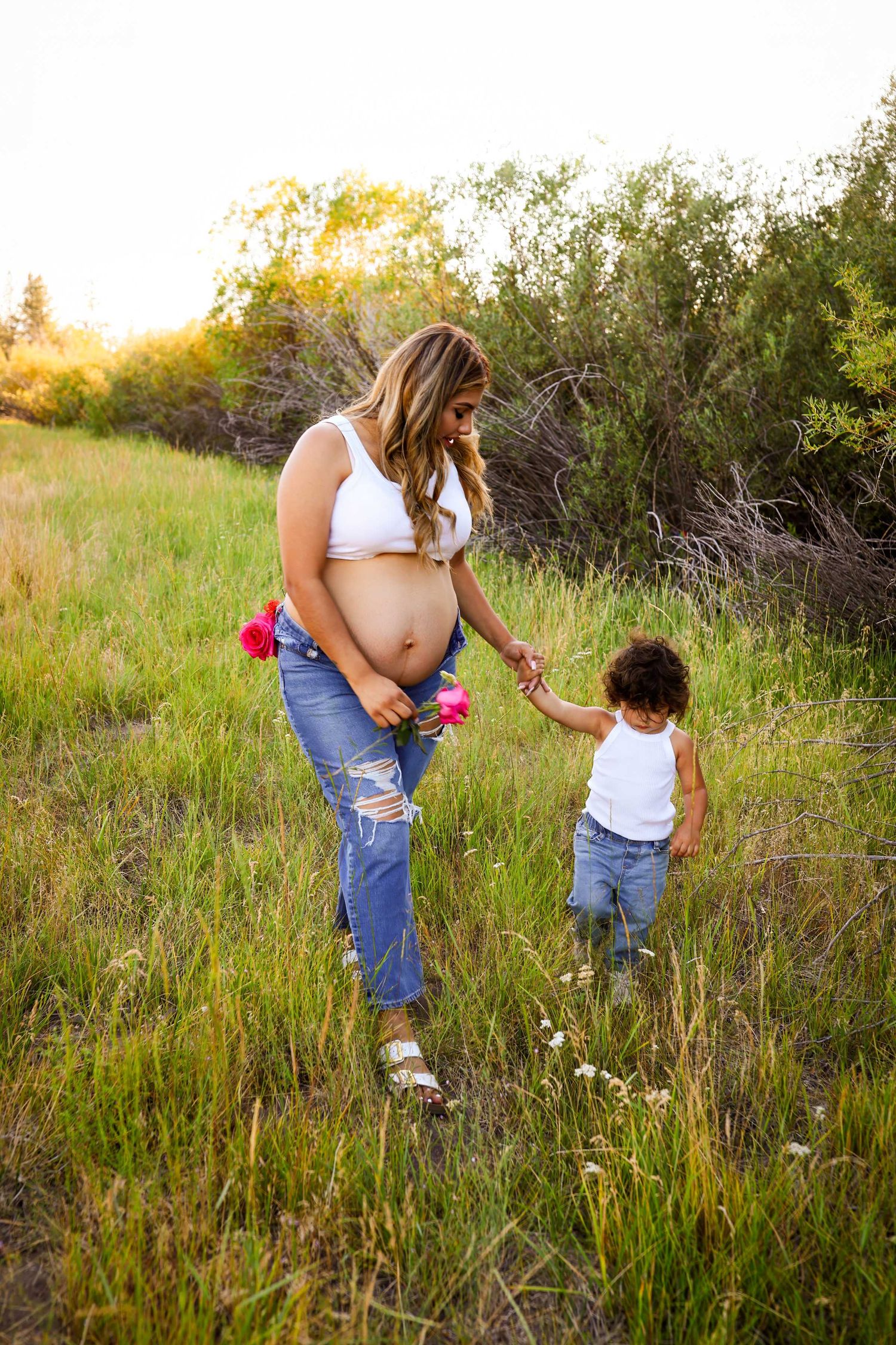Two people explore a grassy meadow together during golden hour, looking at wildflowers and nature.