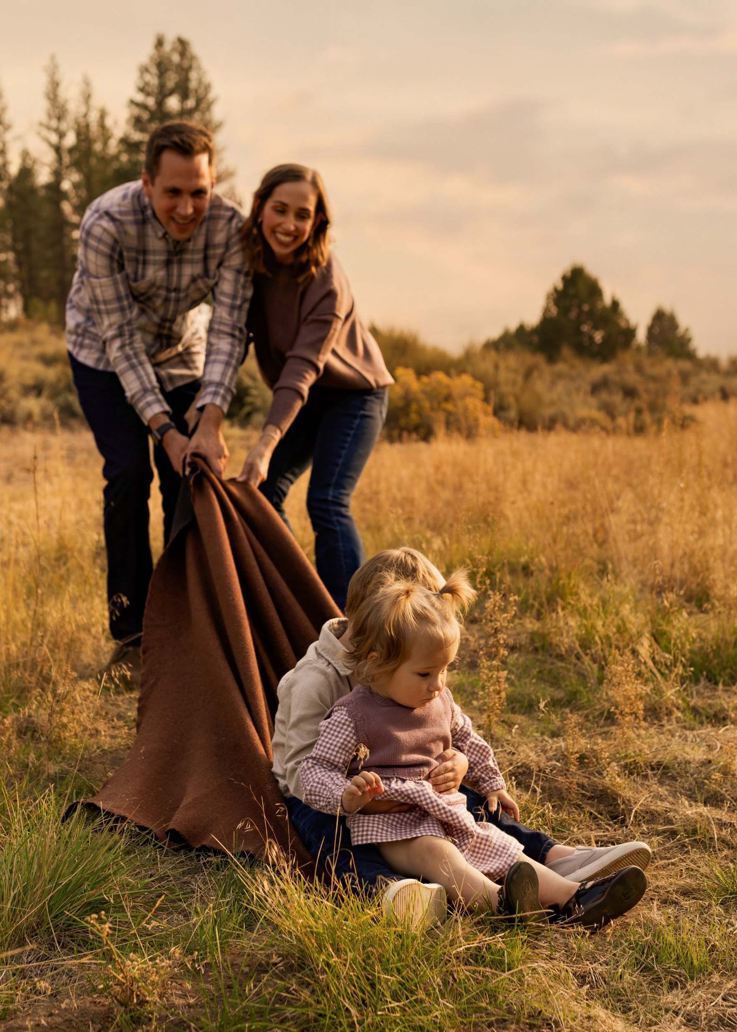 Family relaxing together on grassy hillside during golden hour sunset.