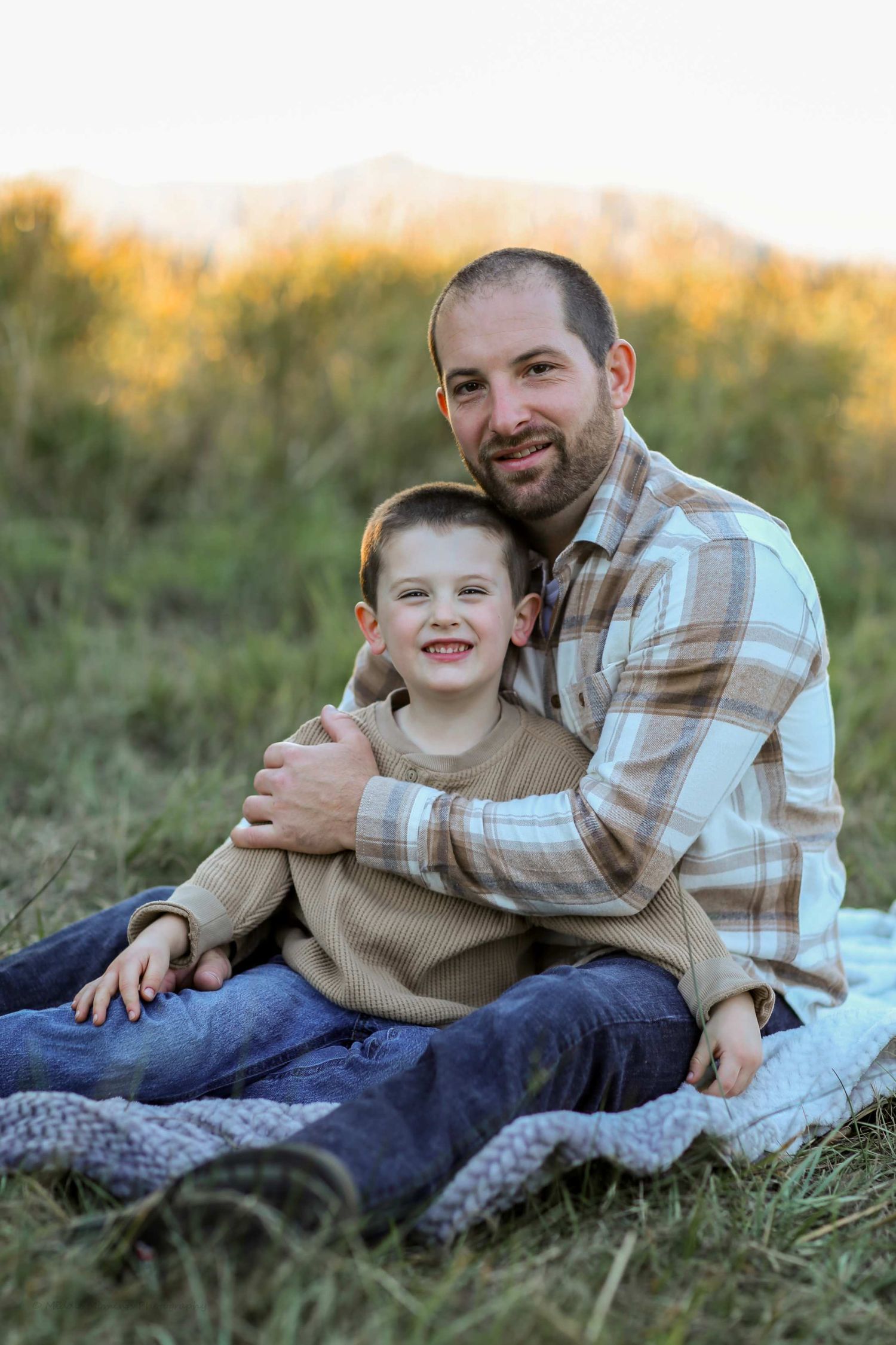 A parent and child share a tender moment while lying in the grass during golden hour sunset.