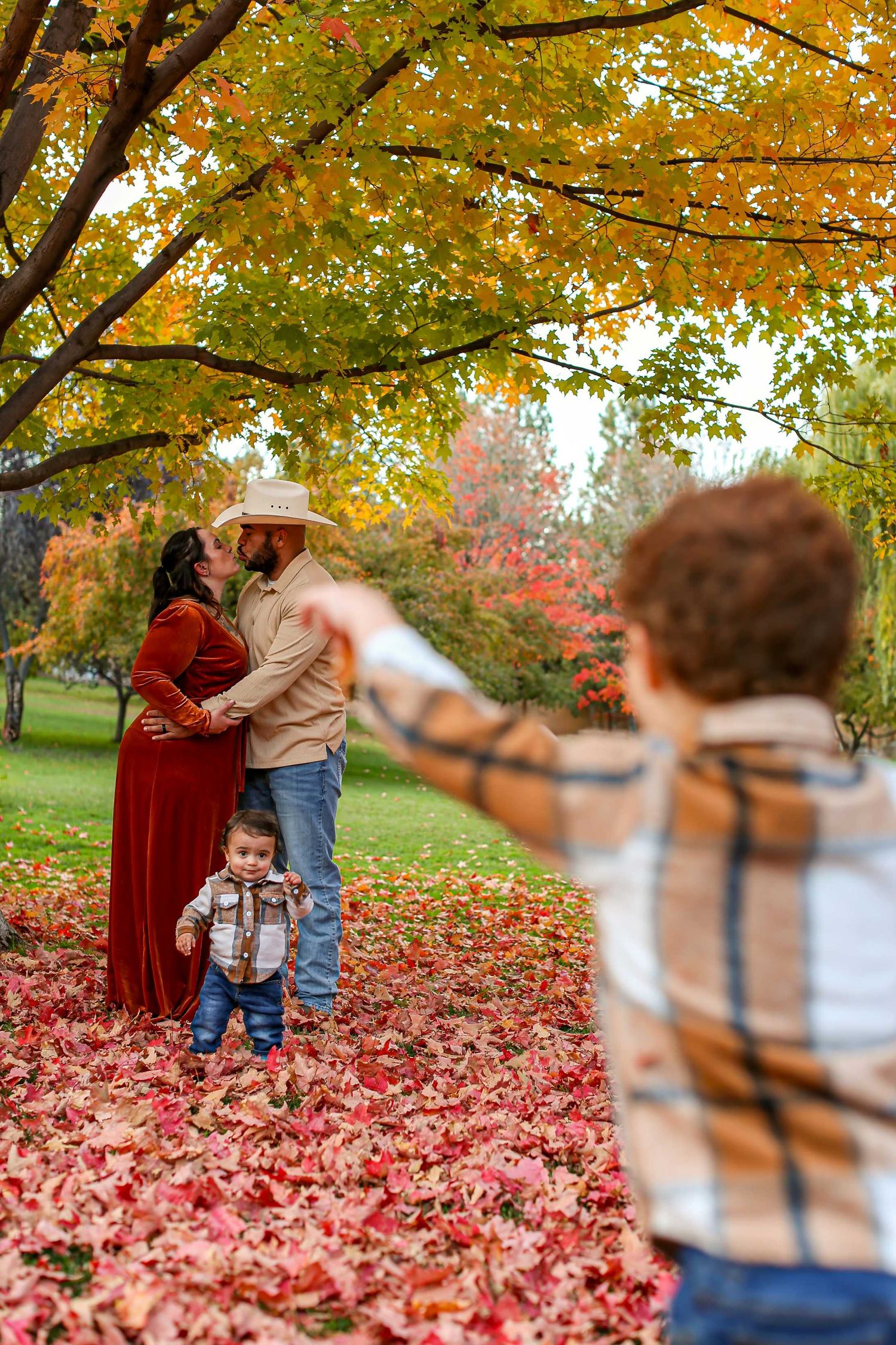 People playing in vibrant red fallen leaves under golden autumn trees in a park.