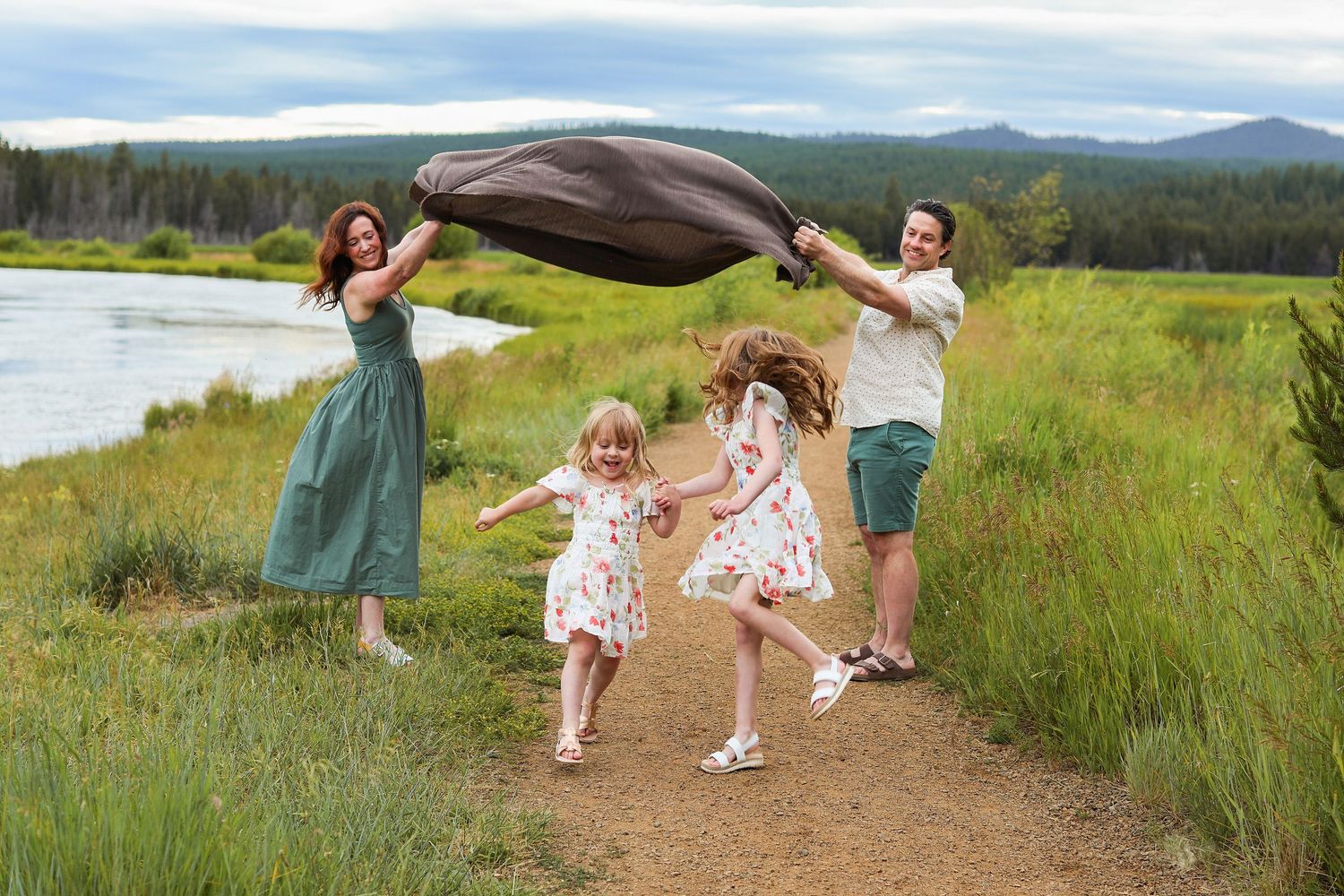 Joyful family playing with a blanket on a scenic meadow trail near a lake and forest. Bend Oregon