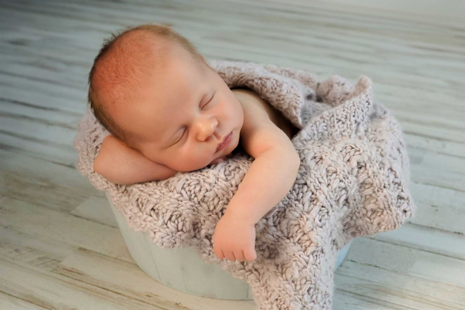 Newborn baby wrapped in lace blanket lying on light wooden floor in progressive poses.