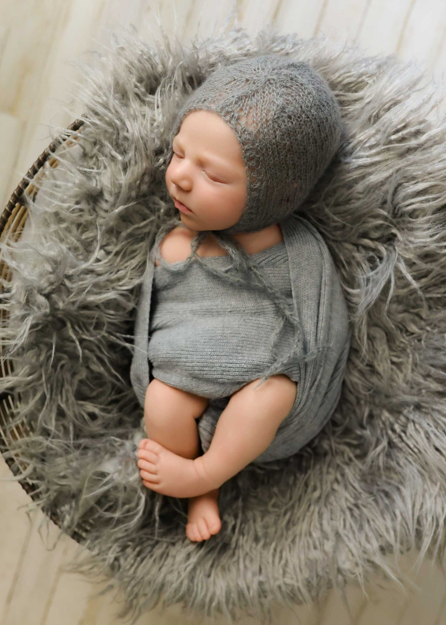 Newborn photography series showing baby in gray outfit lying on soft gray fur blanket.