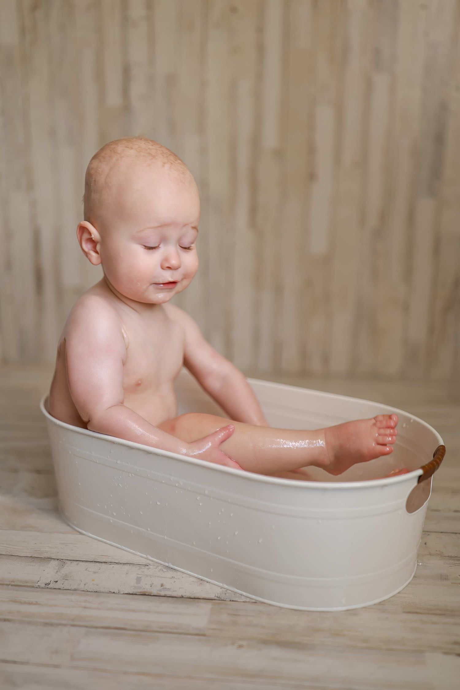 Series of photos showing a baby taking a bath in a white oval tub against a light wooden background.