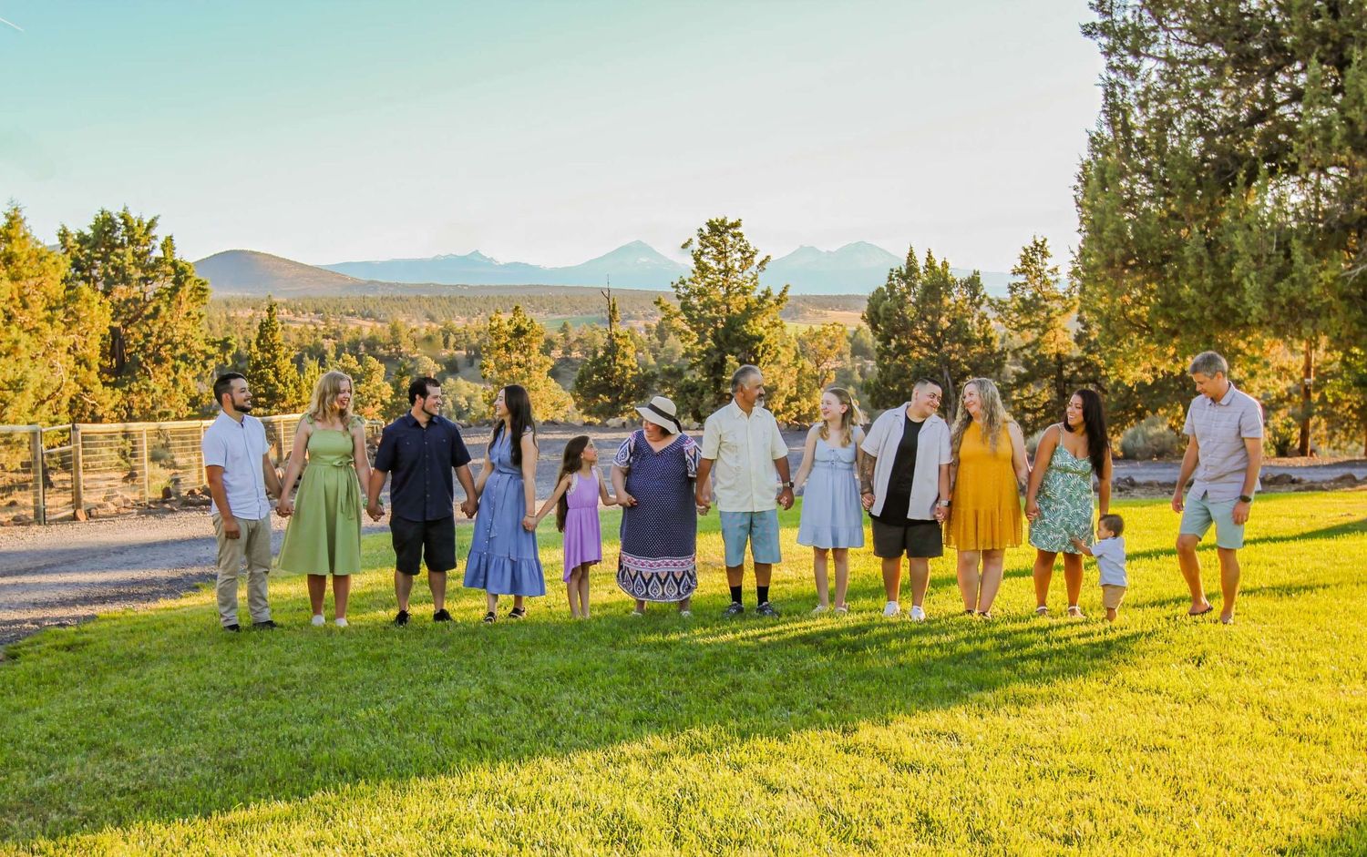 A group stands together on a grassy hillside at sunset with mountains and pine trees in the background.