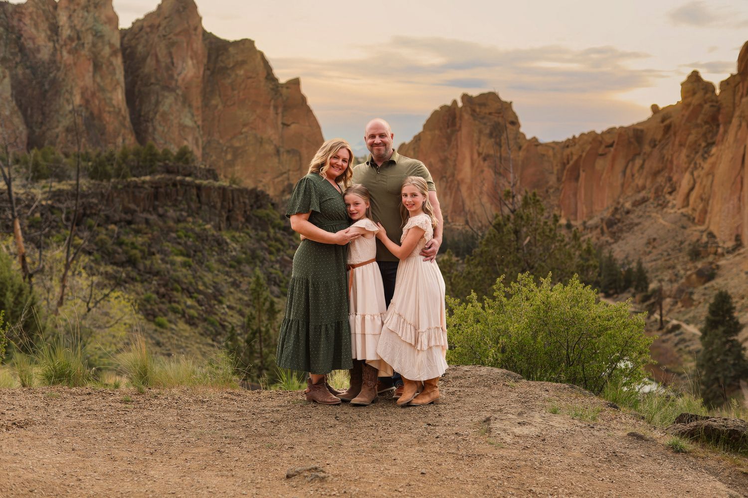 Family of four posing together at Smith Rock State Park, Oregon, with dramatic rocky cliffs at sunset.