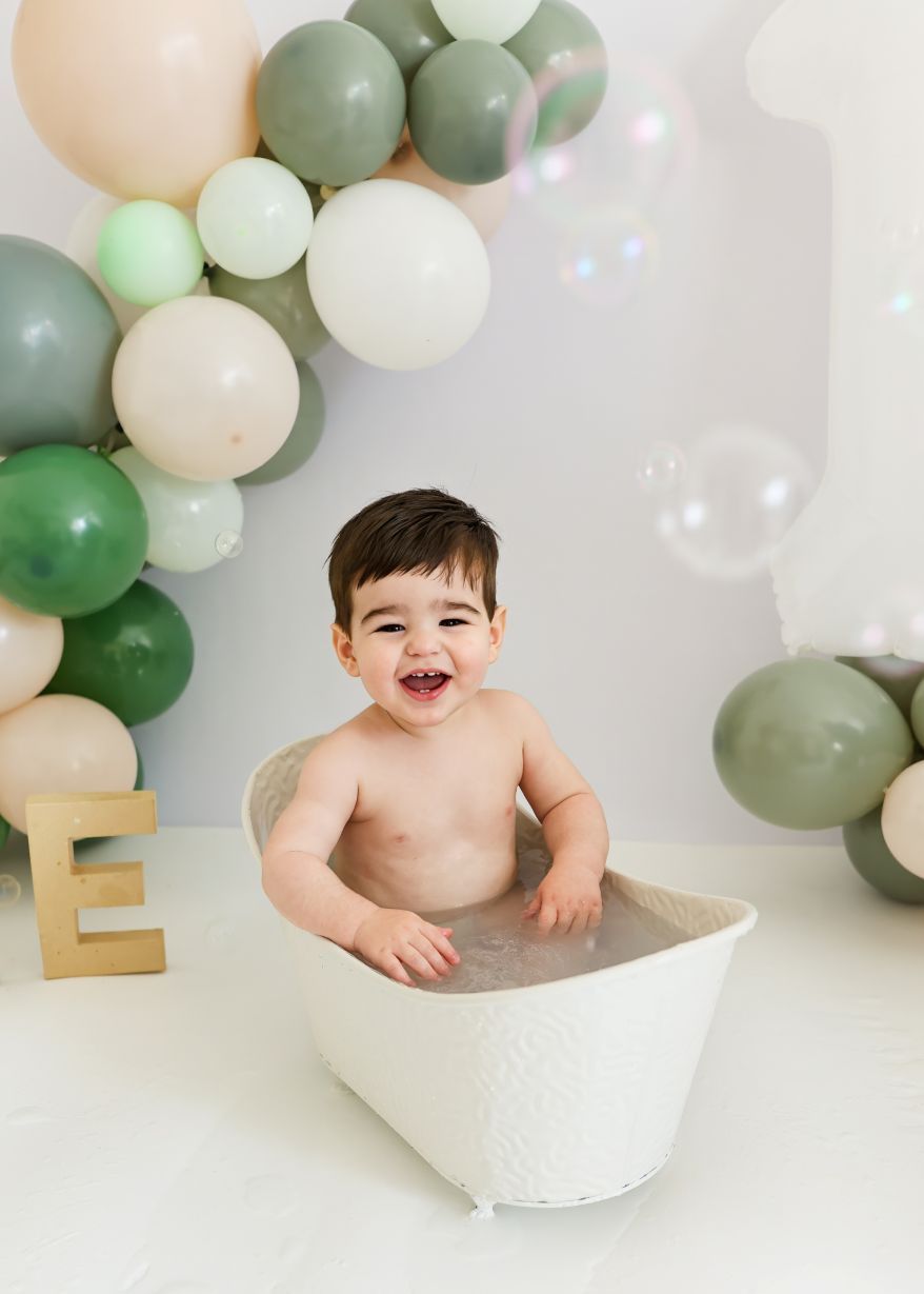 A bath time photo setup with green and cream balloon arch and wooden letter decorations.