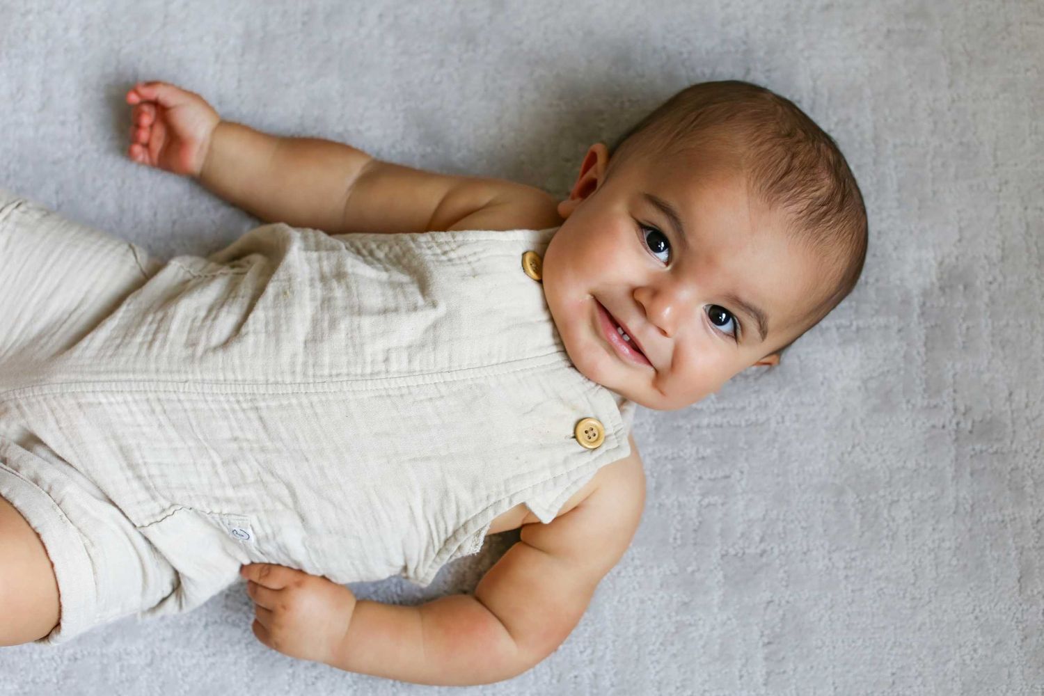 Baby in white outfit lying on soft gray blanket during photo session.