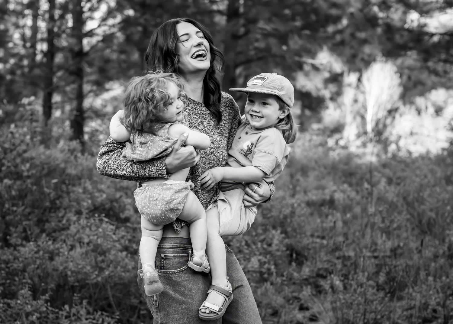Black and white photo of a laughing mother holding two young children outdoors among trees. Shevlin Park Bend Oregon