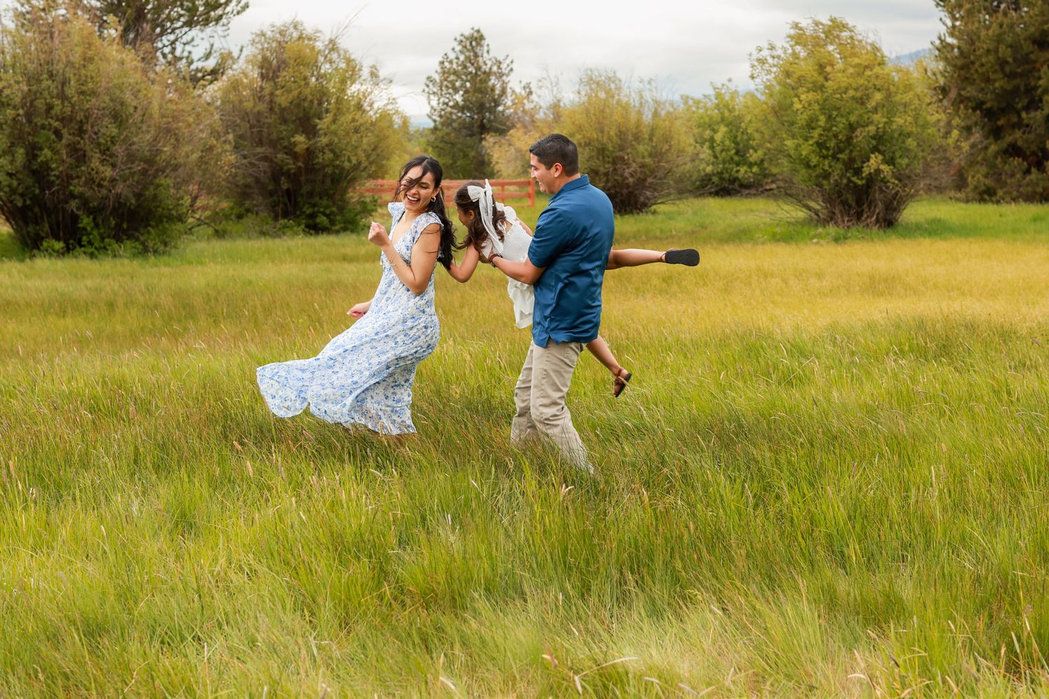 Couple dancing playfully in a green meadow, man holding camera equipment, woman in floral dress, outdoor photography session.