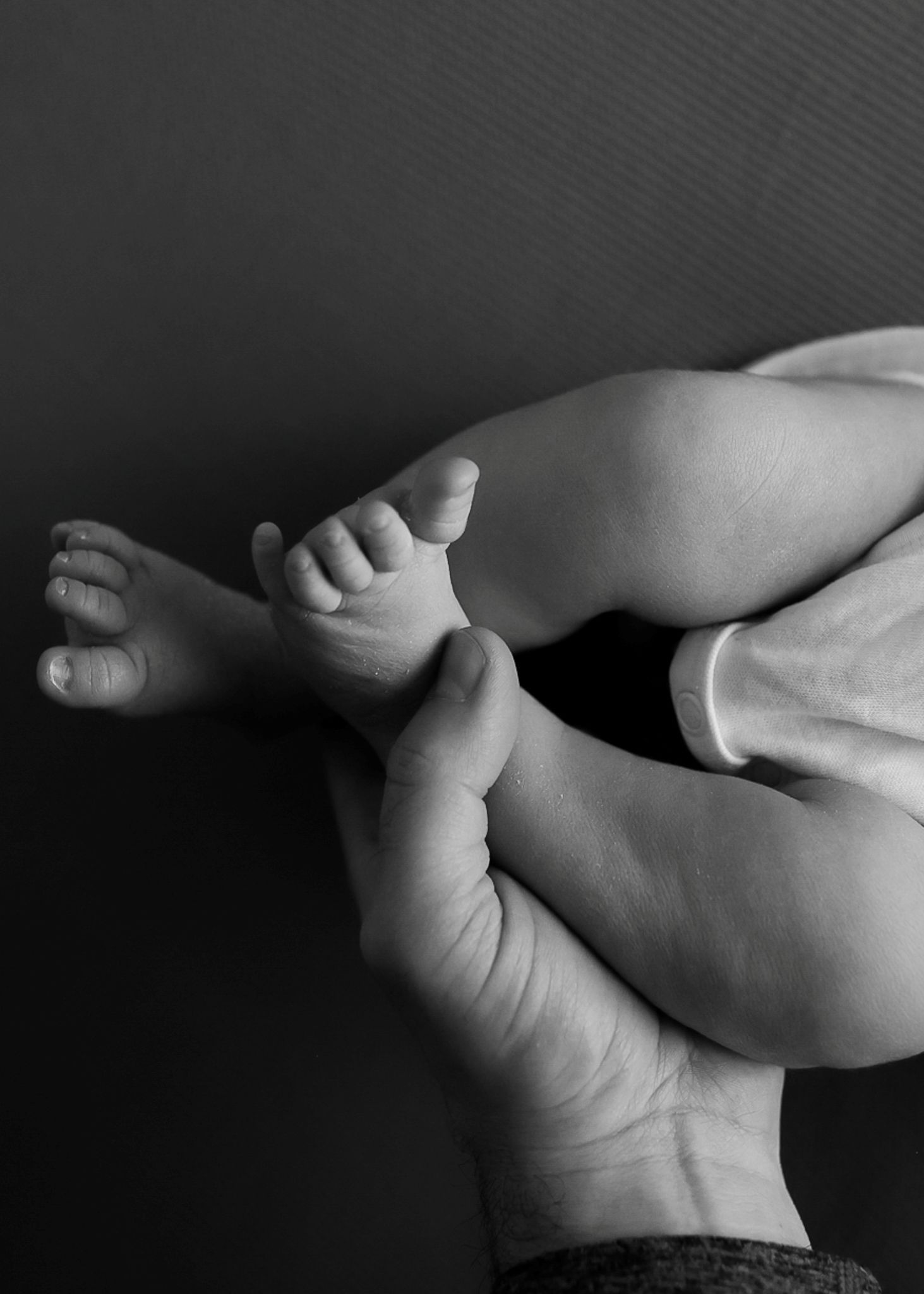 Black and white close-up photograph of tiny baby feet and legs against a dark background. Redmond Oregon Studio