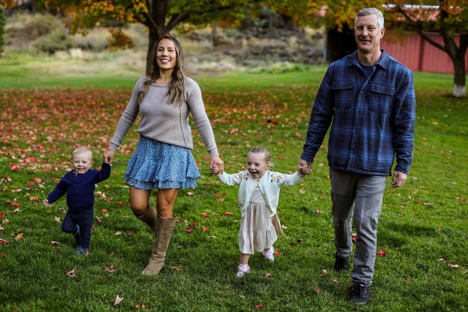 Family walking together and holding hands on autumn grass with colorful fall leaves in a park setting.