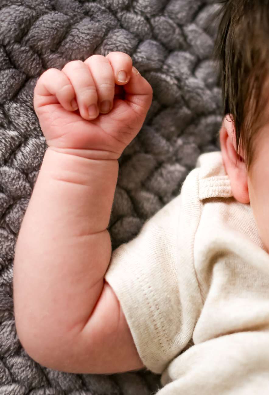 Close-up of baby's tiny fist resting against gray knitted blanket.