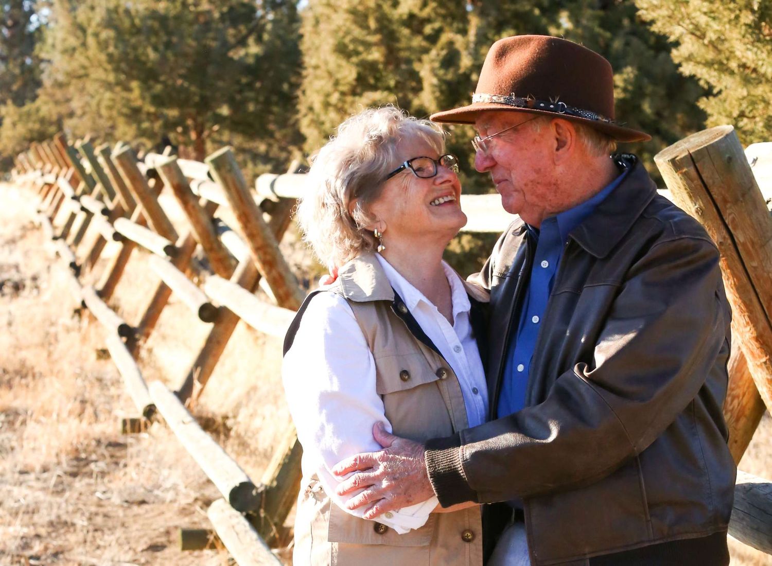 A couple embraces outdoors during a sunny autumn day with trees in the background.