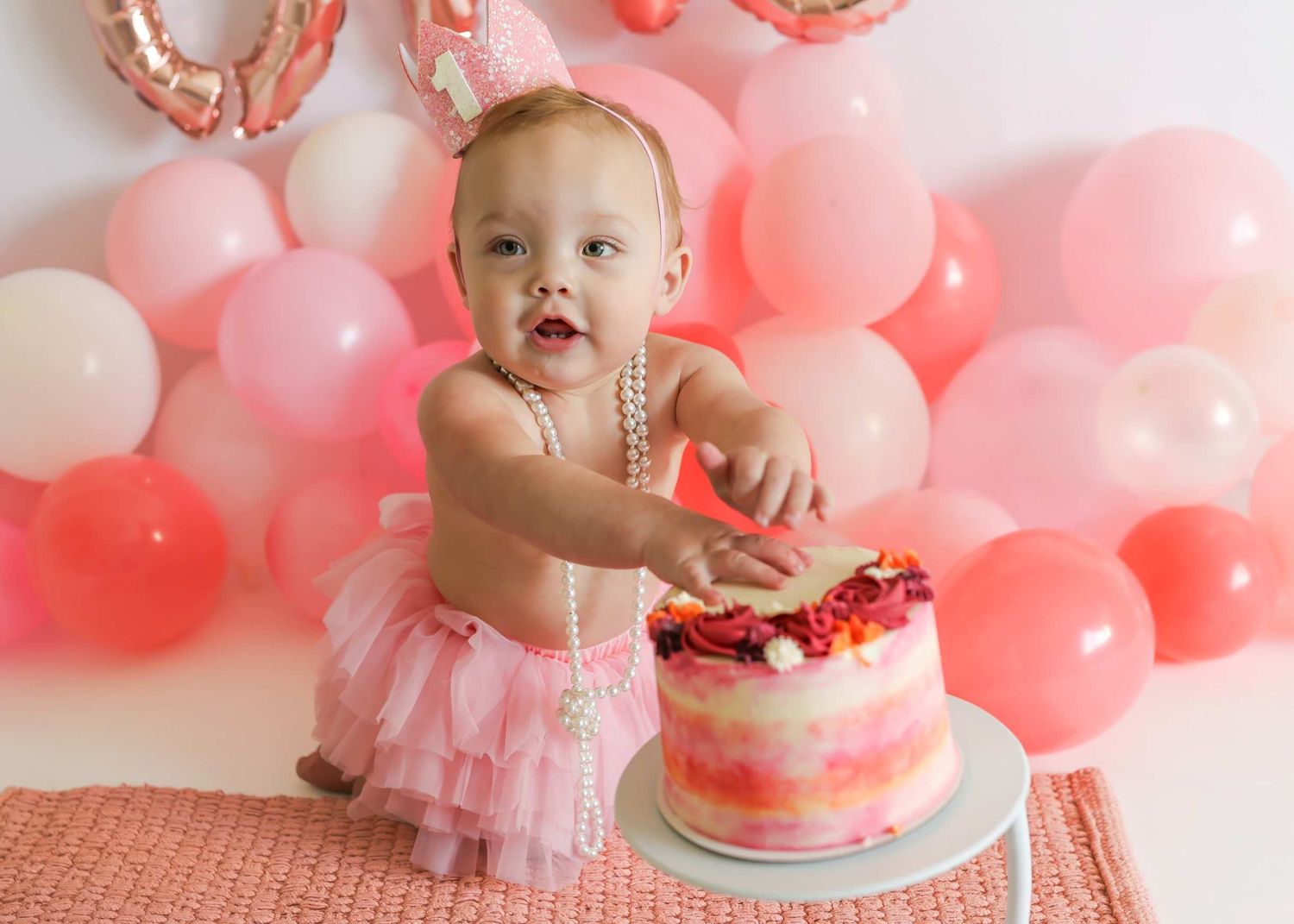 Pink and coral balloon garland with birthday cake and tulle decorations for first birthday celebration.