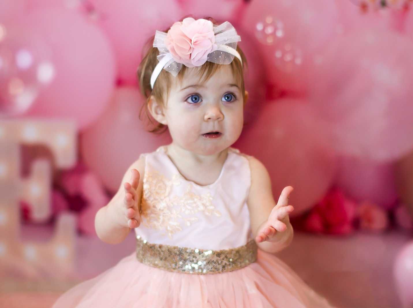 Baby in pink tulle dress against pink floral backdrop with sparkly details.