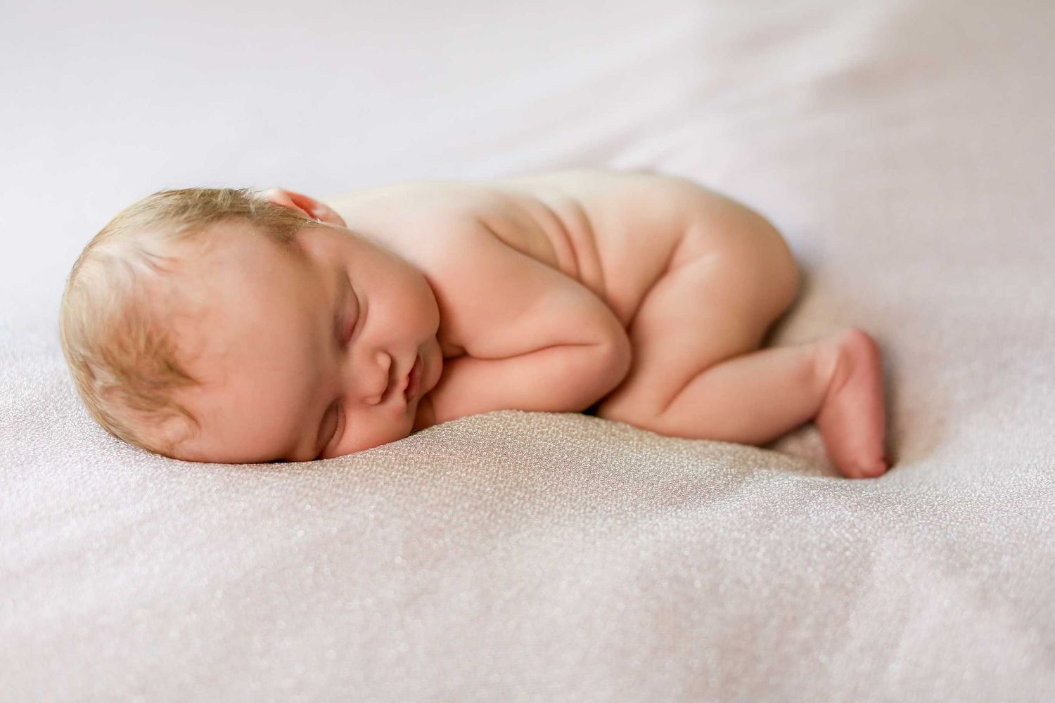 Serene newborn sleeping on white blanket during professional photography session.