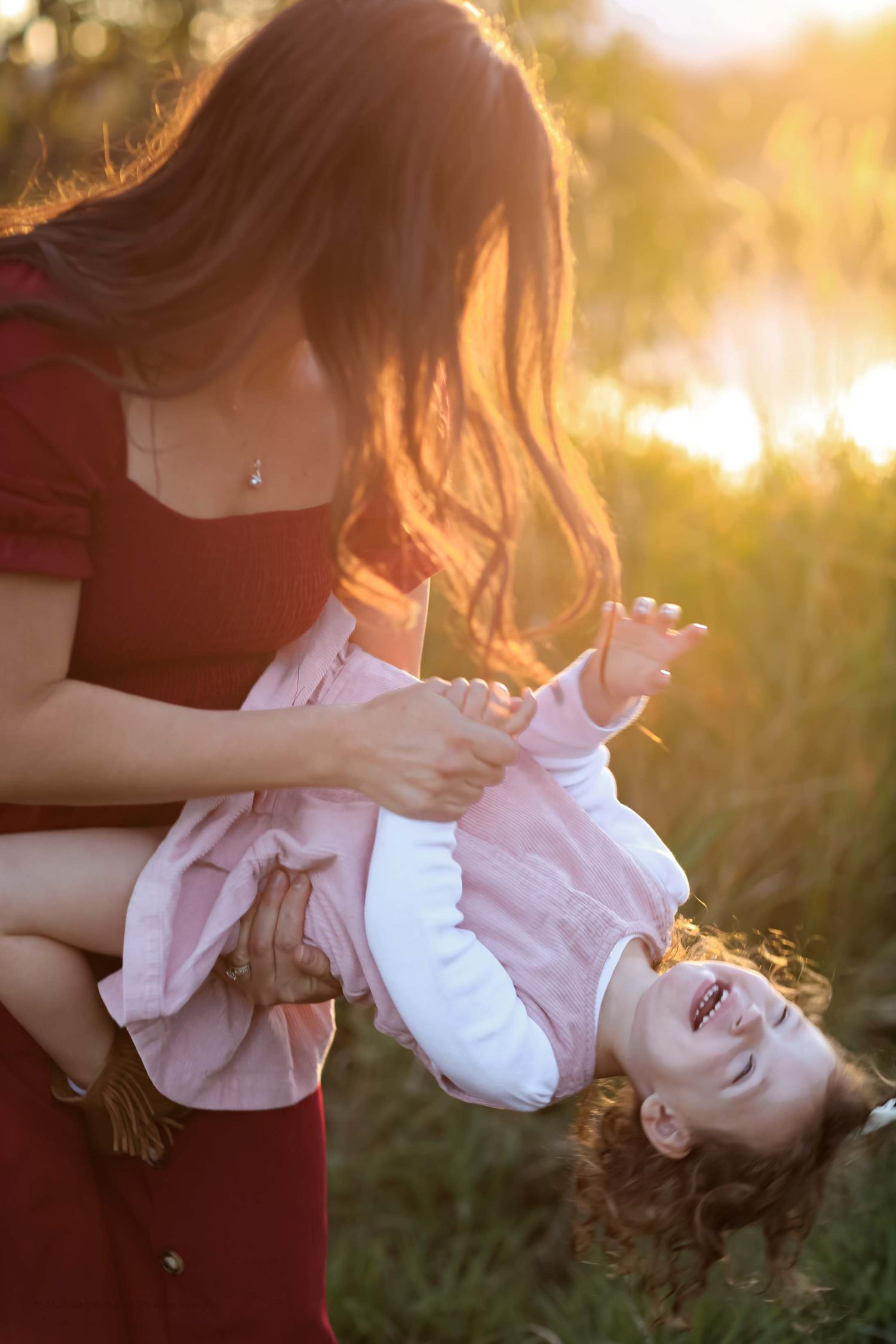 A tender moment between parent and child silhouetted against a warm golden sunset in a grassy field.