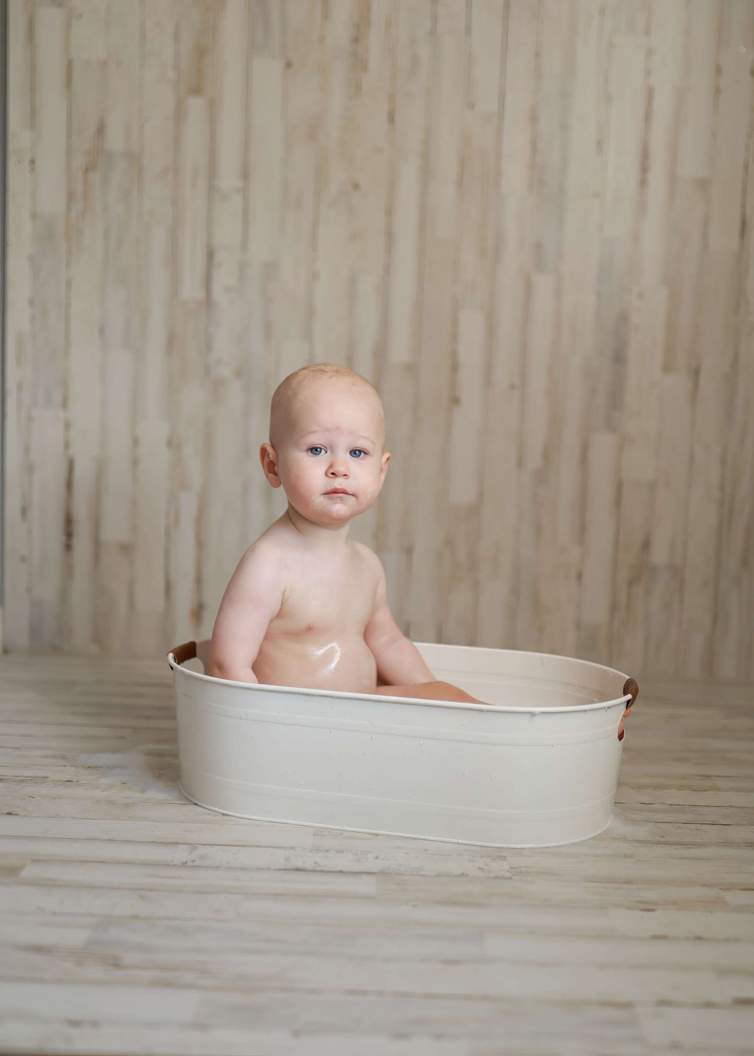 Progressive shots of an infant sitting in a white bathtub on a wooden floor during bathtime.