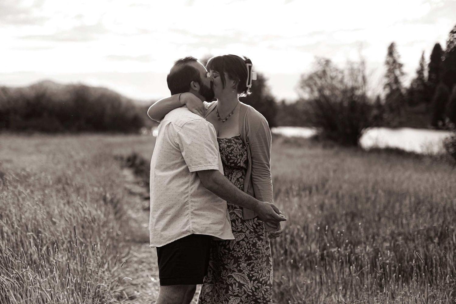 A romantic black and white photo of a couple embracing in a serene meadow with mountains in the background.