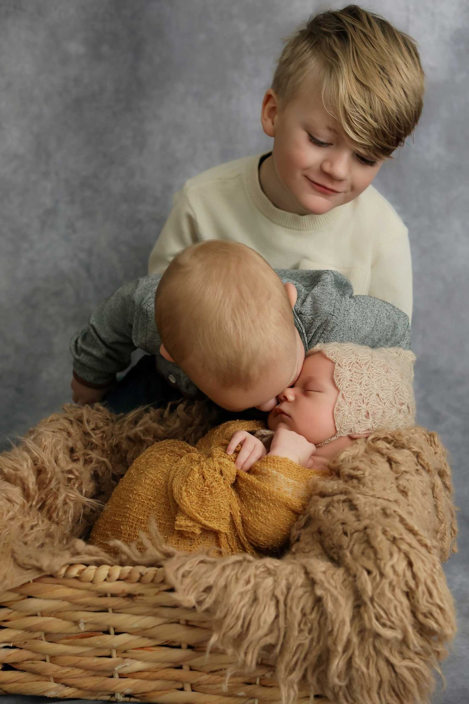 Sweet sibling portrait showing gentle interaction on a brown textured backdrop.