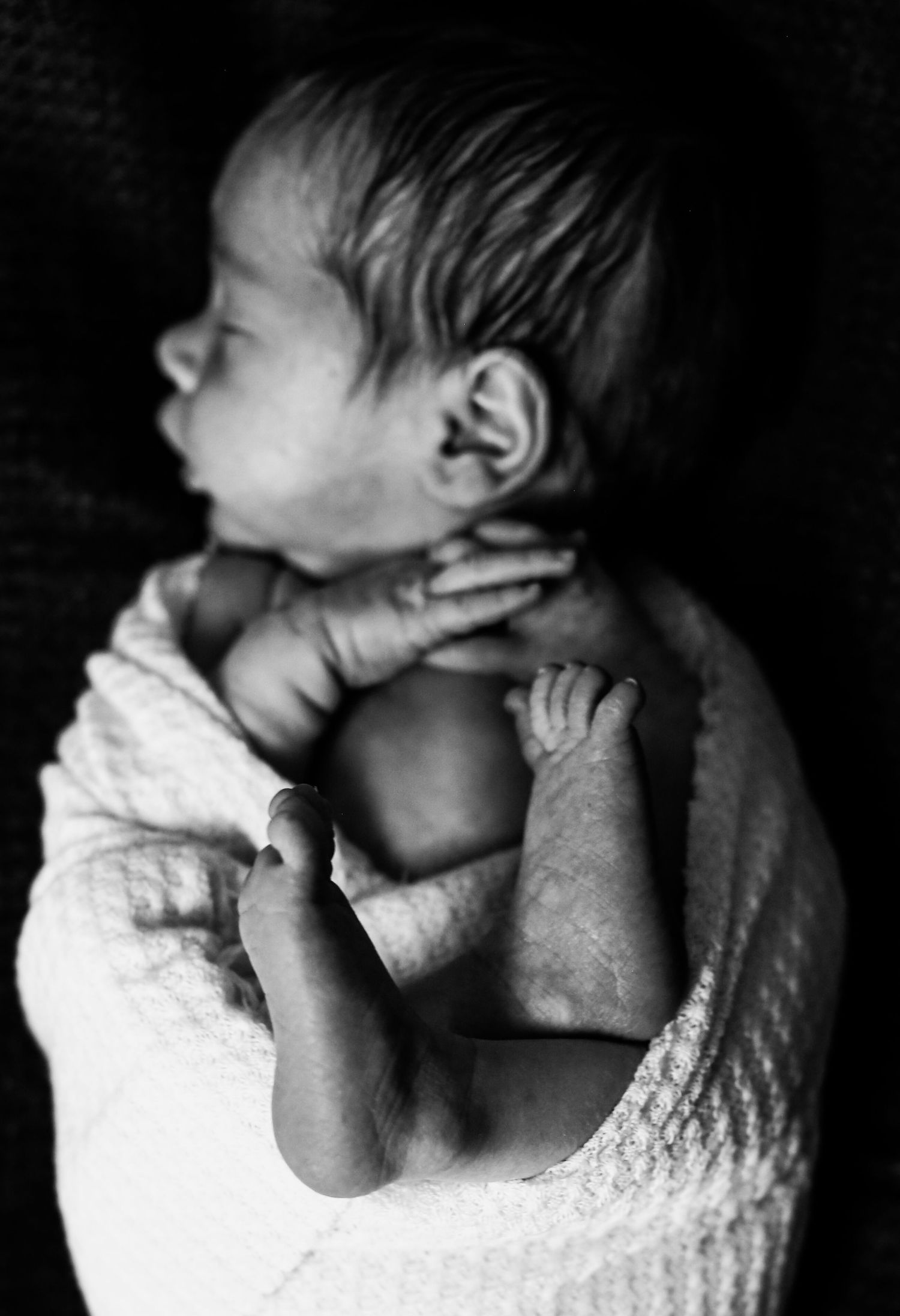Artistic black and white portrait of newborn wrapped in soft textured blanket.