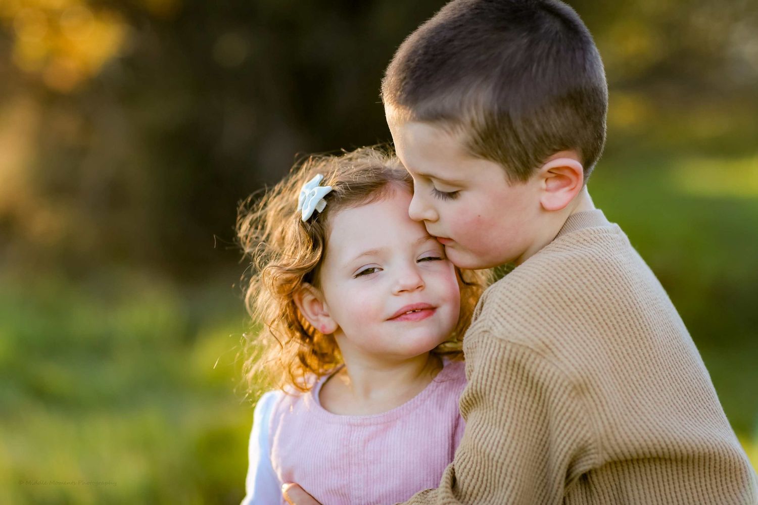A couple embraces outdoors during golden hour while sharing tender moments in a romantic photo session.
