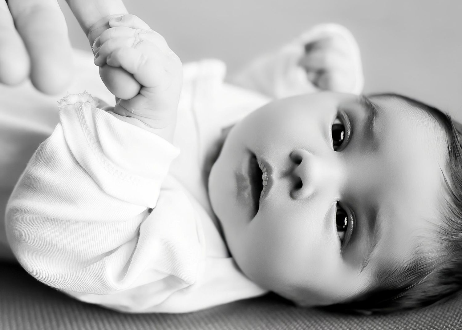 Black and white portrait of baby in white outfit looking up with bright eyes.