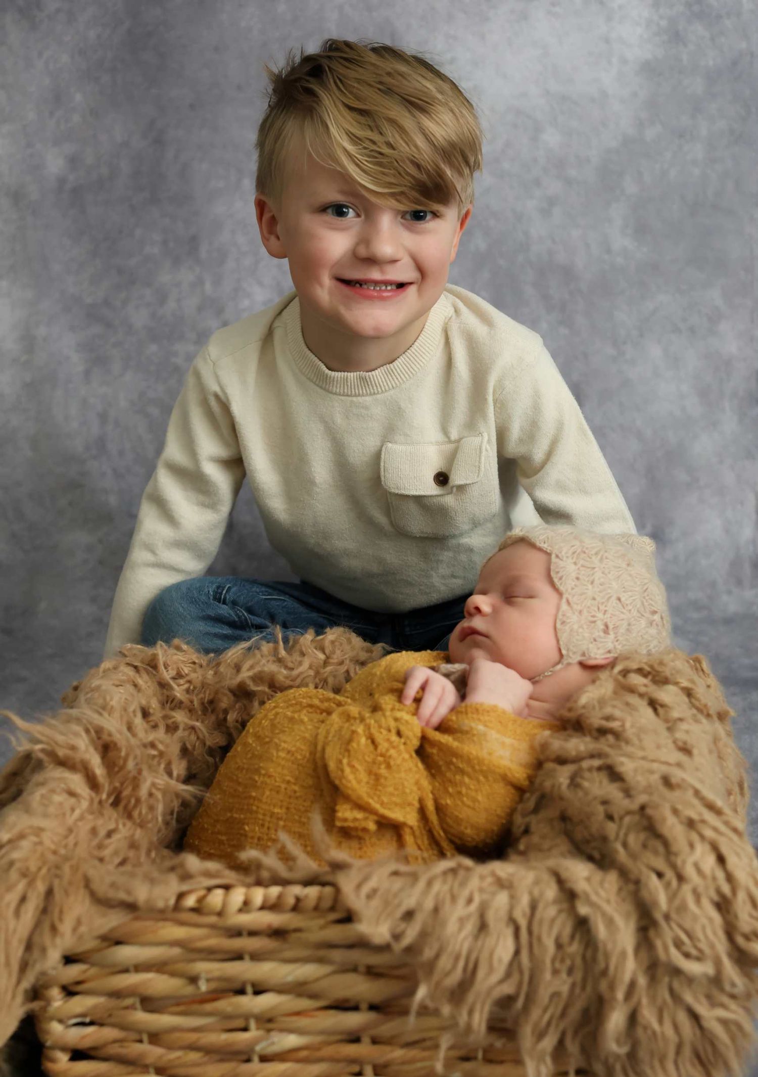 Siblings share a tender moment on a textured beige blanket during a professional photoshoot.