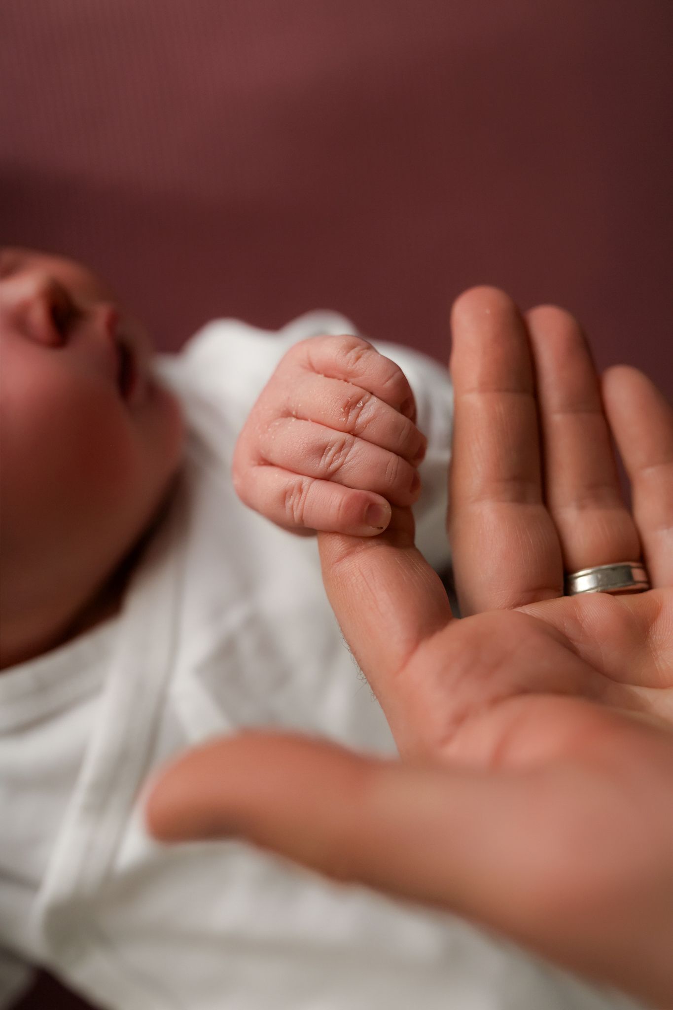 Close-up of tiny baby fingers grasping adult finger with wedding ring visible.