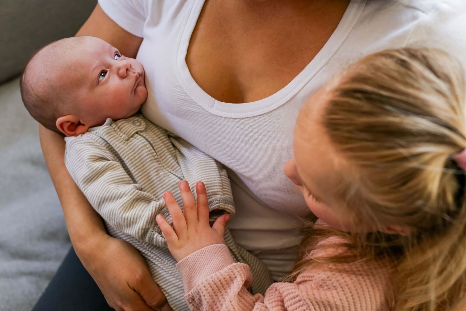 Mother in white tank top tenderly holding and bonding with newborn baby against neutral background.