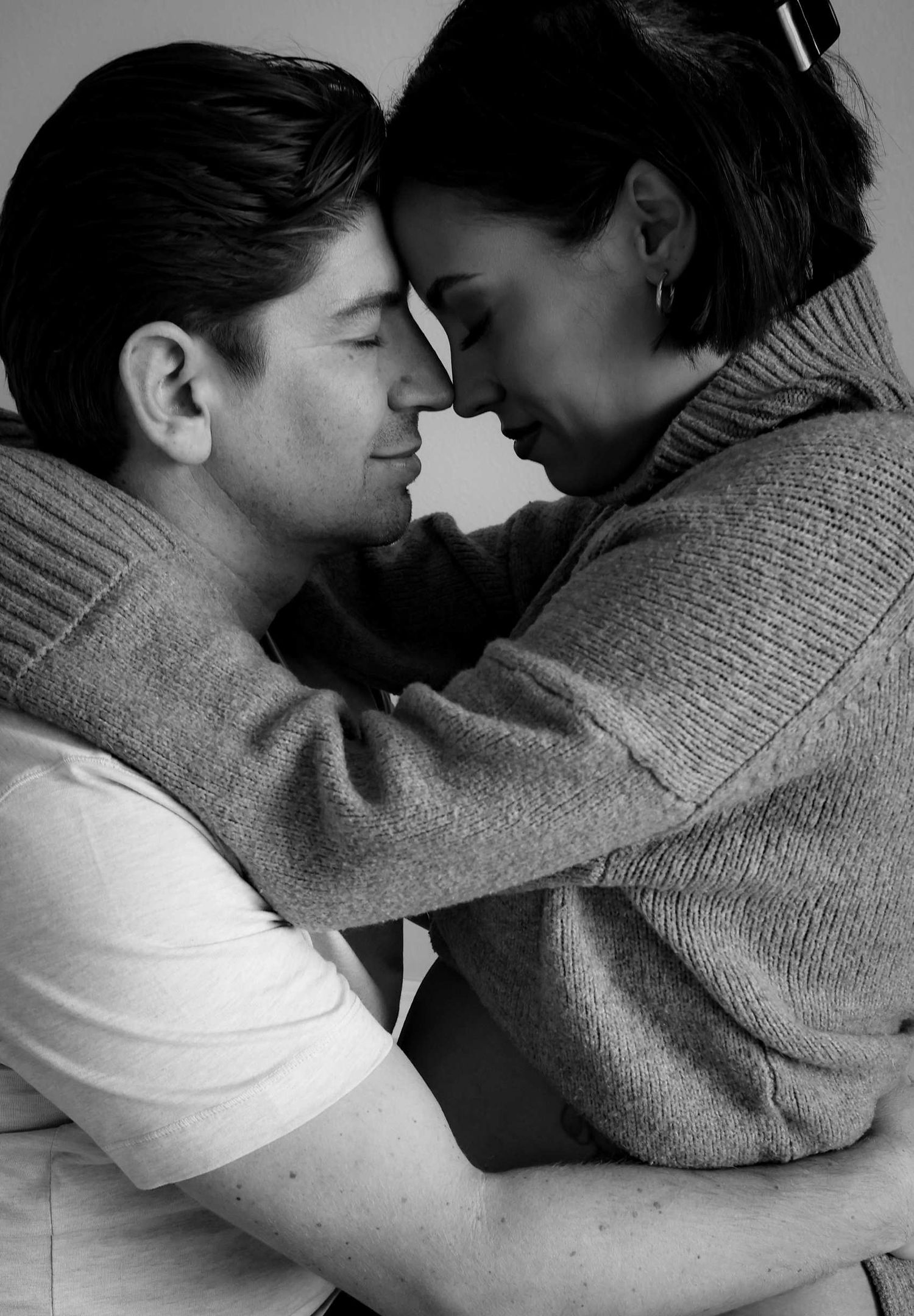 Intimate black and white portrait of couple in sweaters sharing close romantic moment.